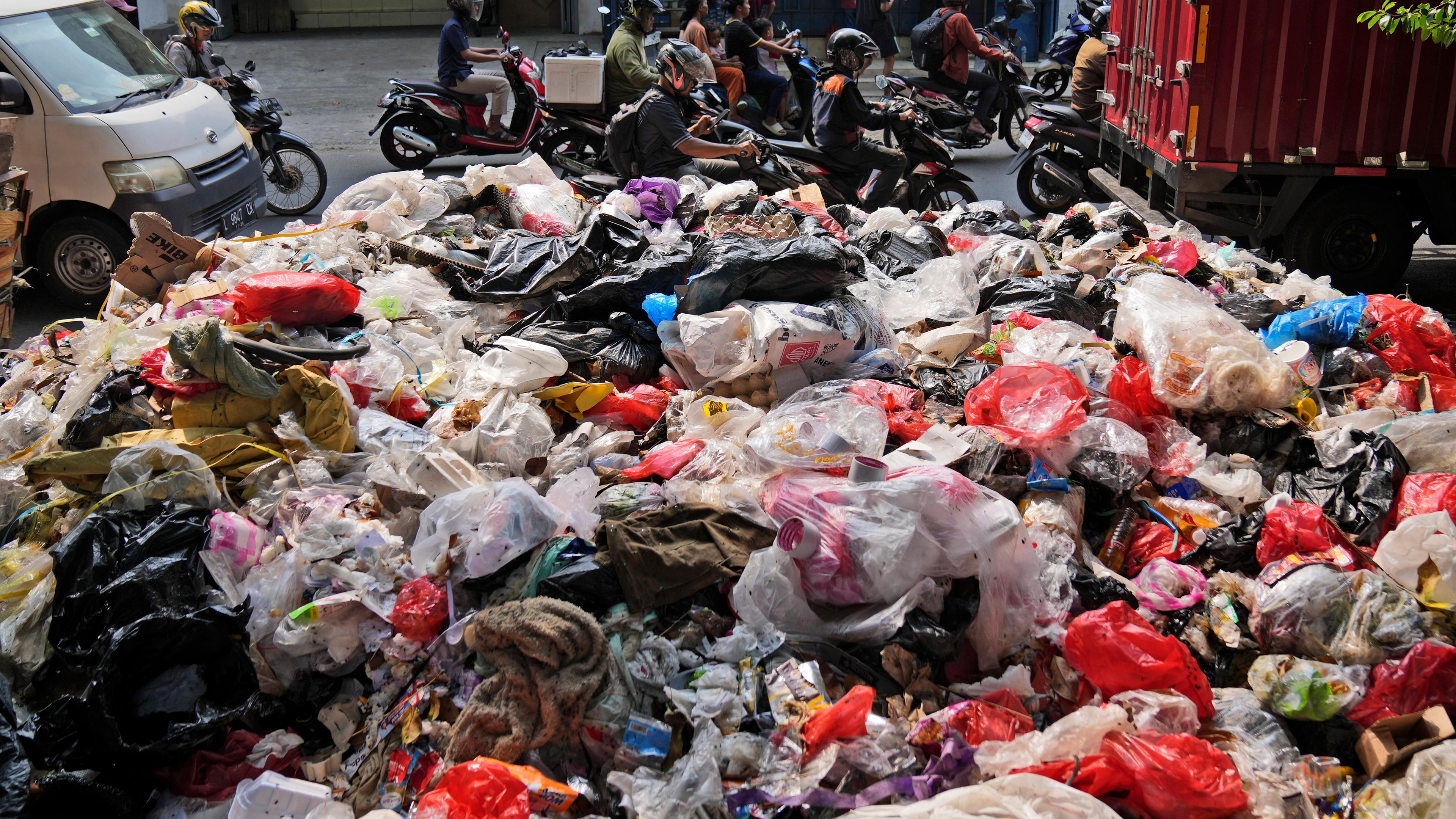 Autofahrer fahren am Straßenrand aufgetürmten Müll vorbei, der größtenteils aus Plastik besteht. 