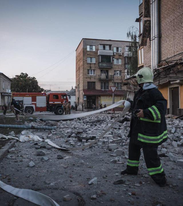 Eine Einsatzkraft der Feuerwehr hält inmitten von Trümmern einen Schlauch in der Hand.