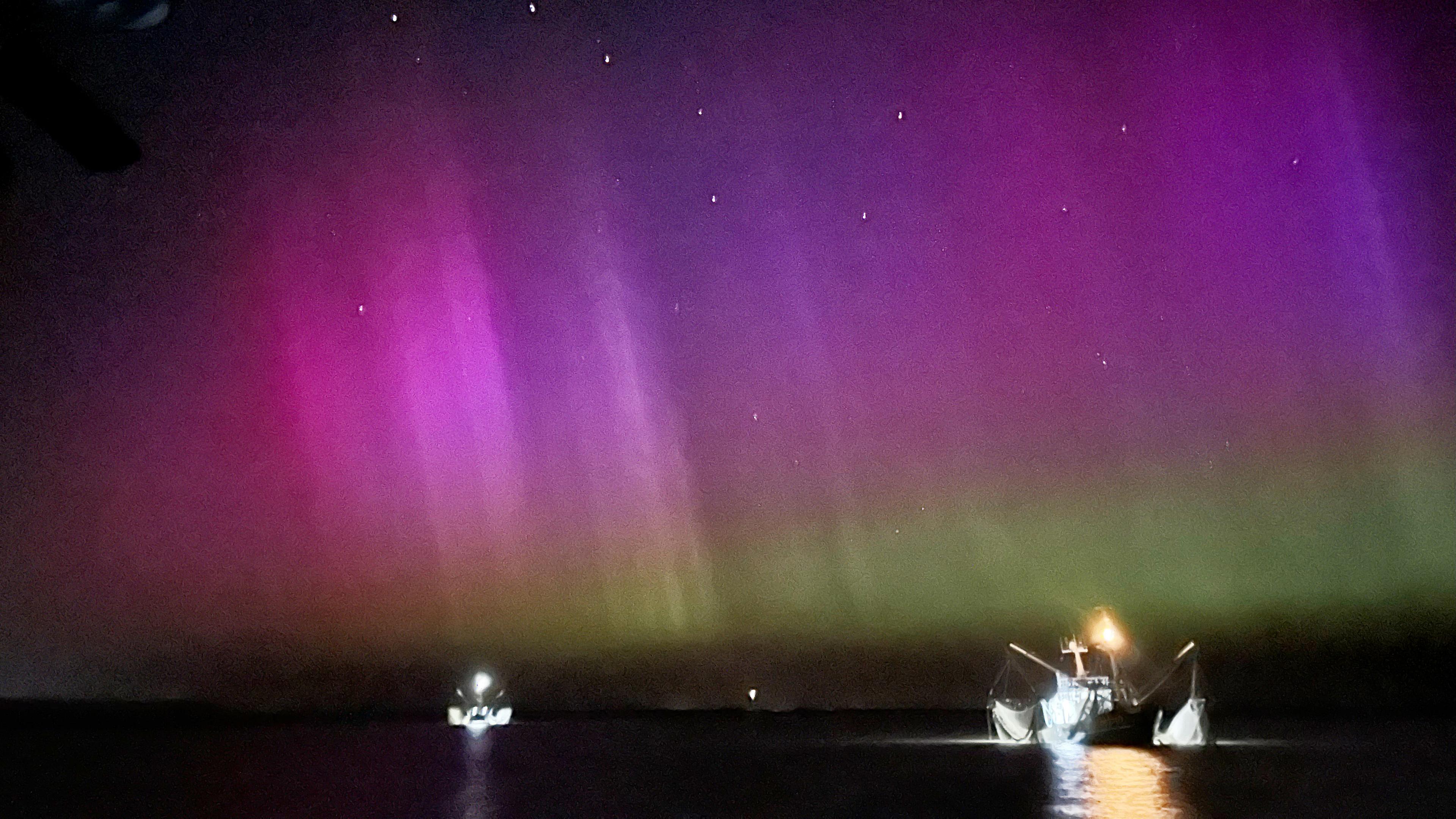 Niedersachsen, Borkum: Zwei Krabbenkutter fahren am frühen Morgen über die Nordsee in der Nähe von Borkum, während Polarlichter am Himmel zu sehen sind.