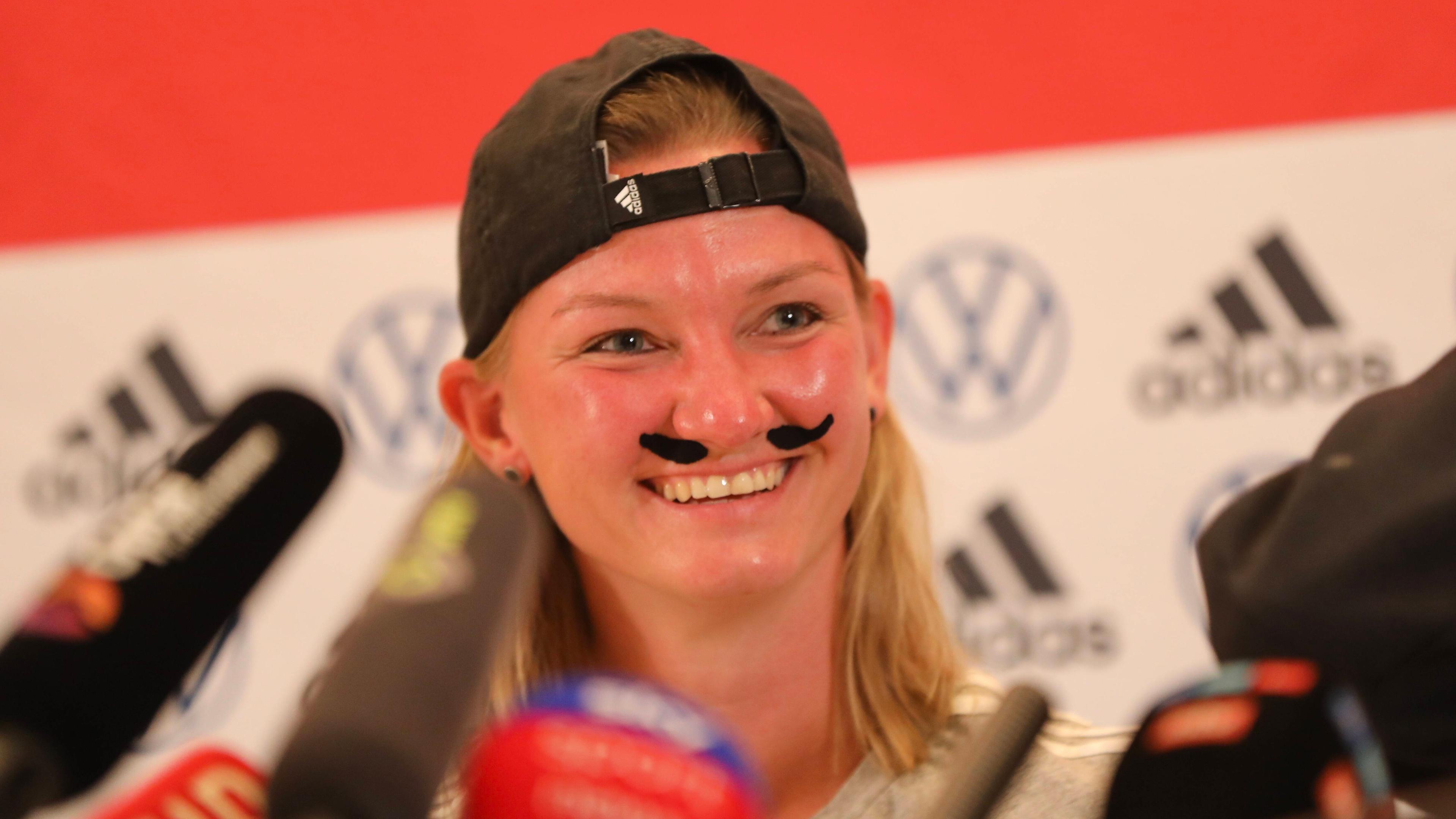 Die Kapitänin Alexandra Popp kommt bei der Pressekonferenz mit Schnurbart und Kappe nachdem sie im Internet als Alexander Bopp bezeichnet wurde.