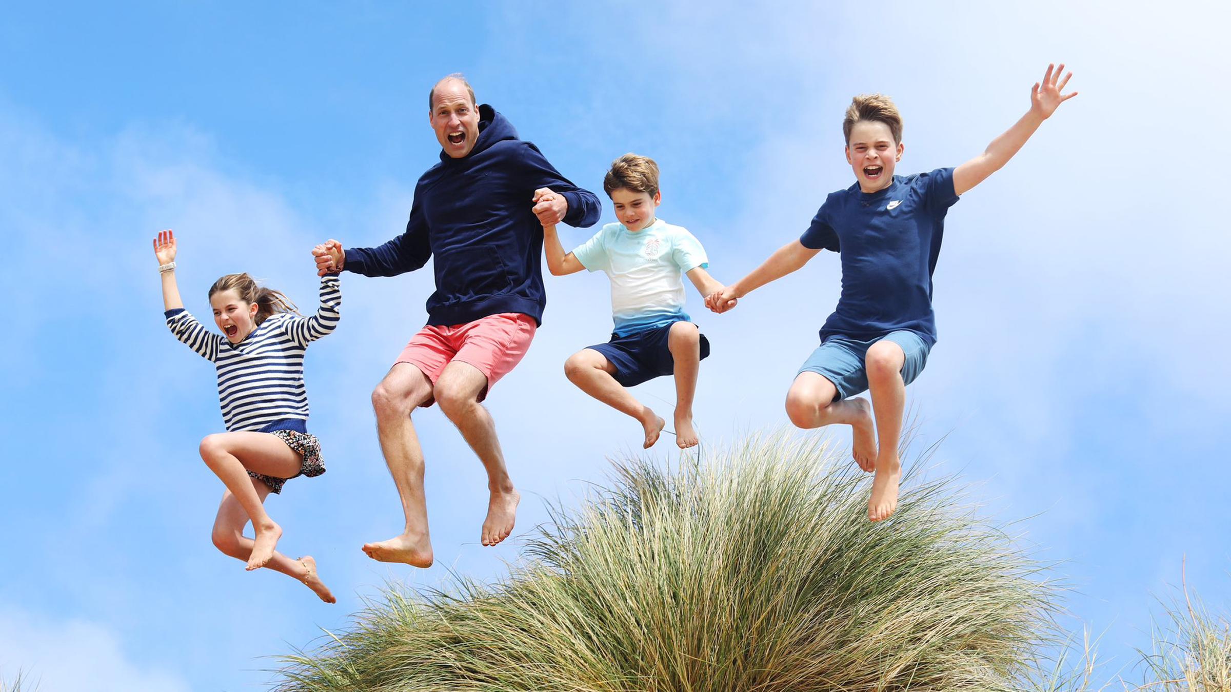 Prinz William springt mit seinen Kindern, Charlotte, Louis und George, über eine Düne.