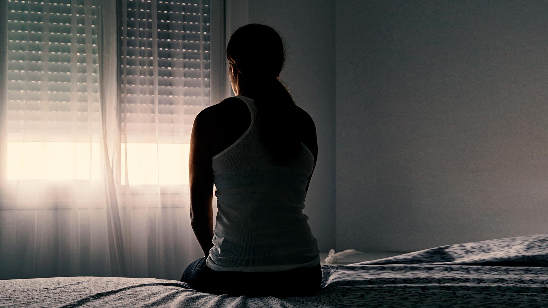 Eine Frau sitzt auf einem Bett in einem dunklen Raum