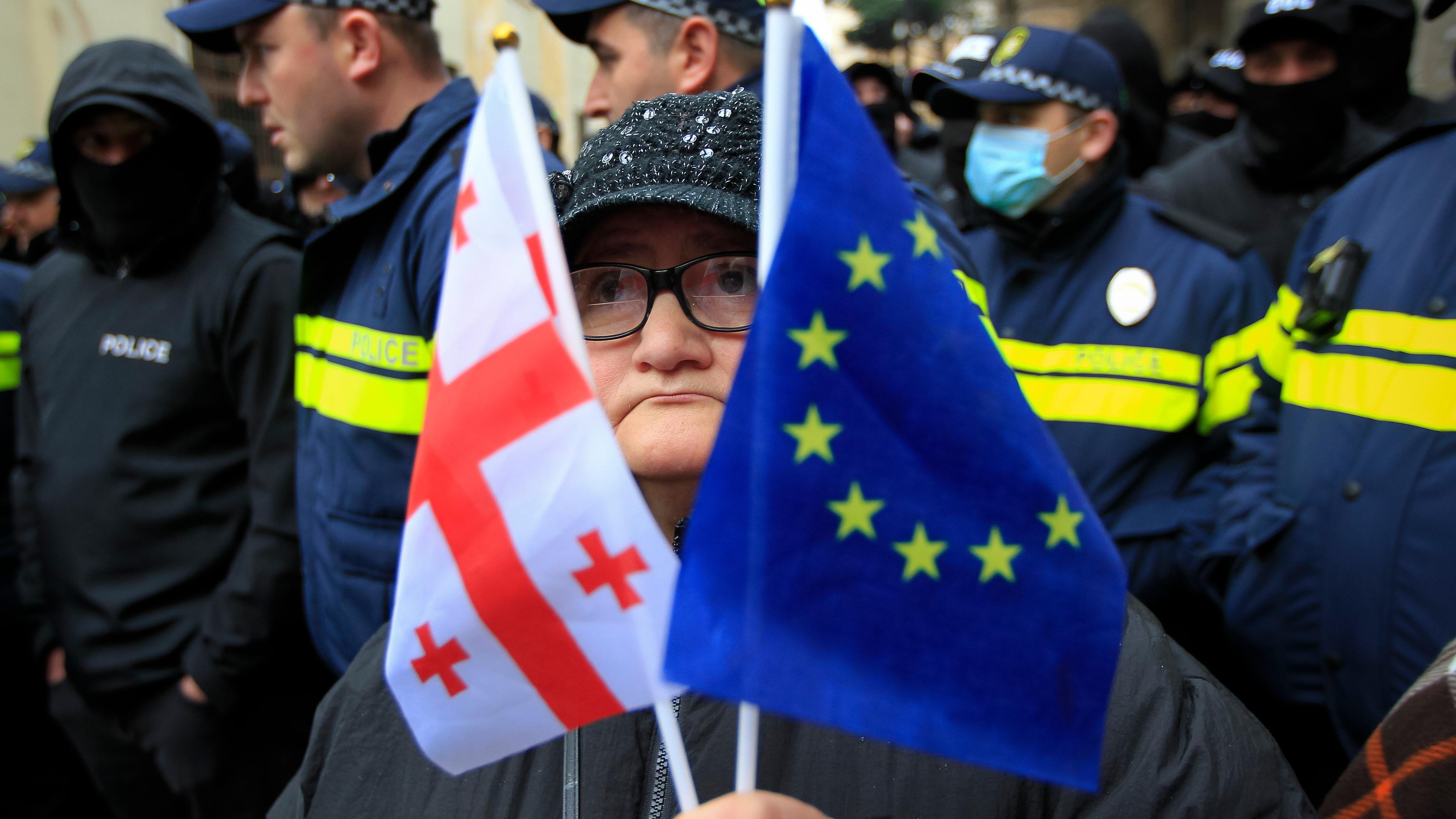 Eine Frau mit einer EU- und einer georgischen Nationalflagge steht vor der Polizei.