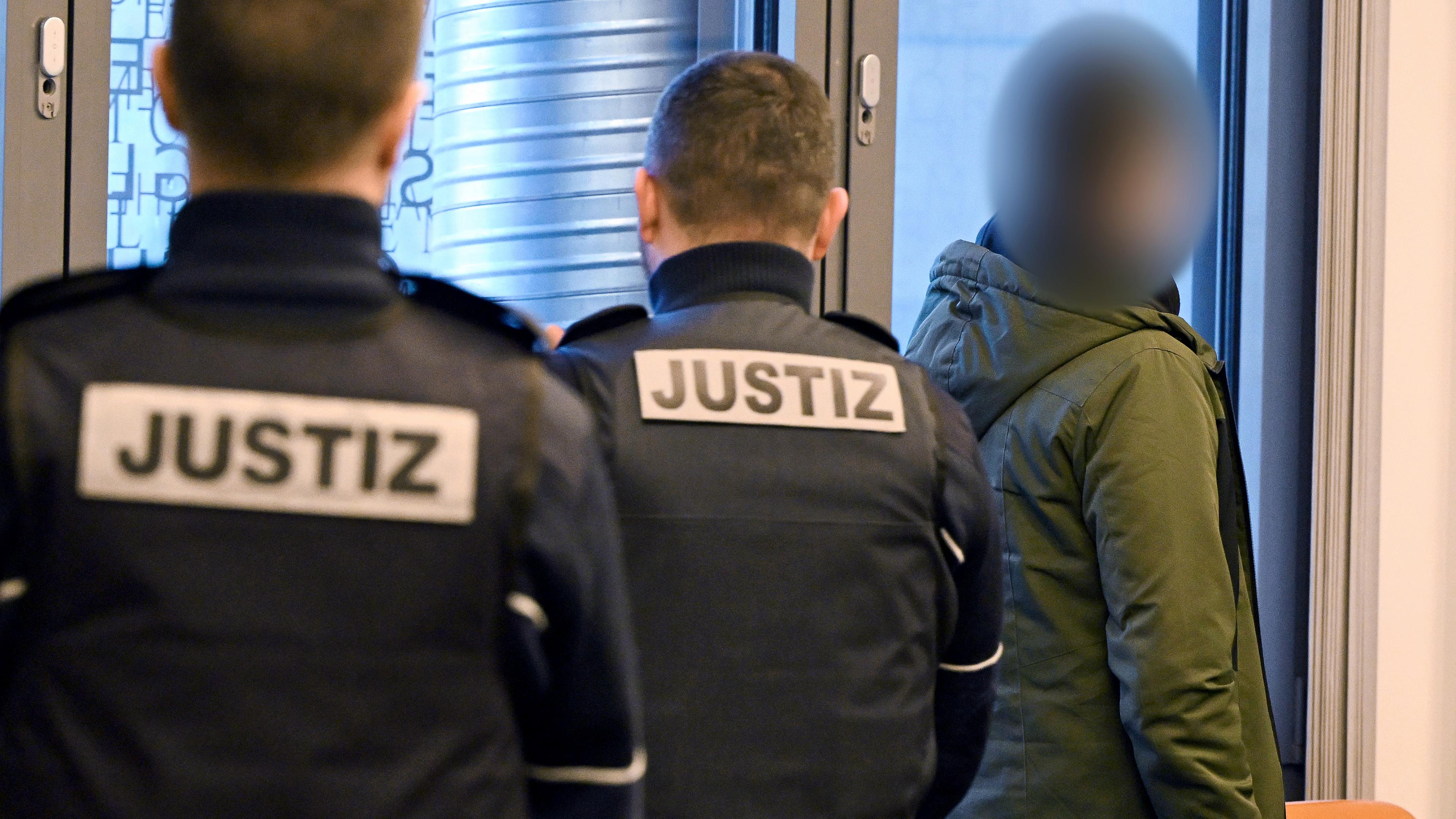 Der Angeklagte (r.) geht vor zwei Justizbeamten in den Gerichtssaal