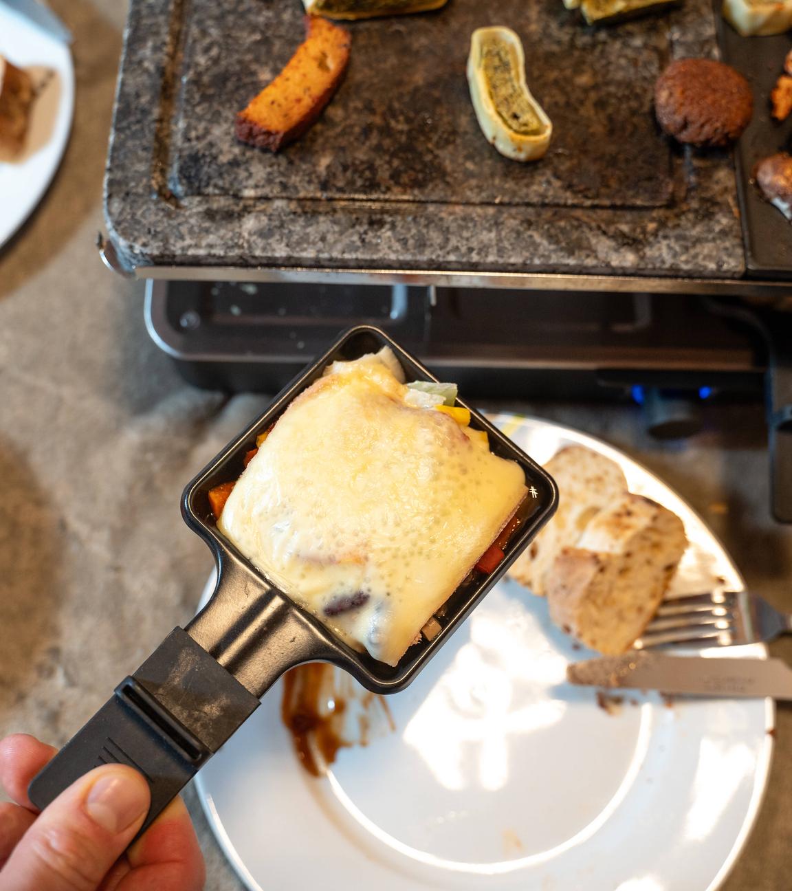 Mann hält Raclette-Pfännchen in der Hand.