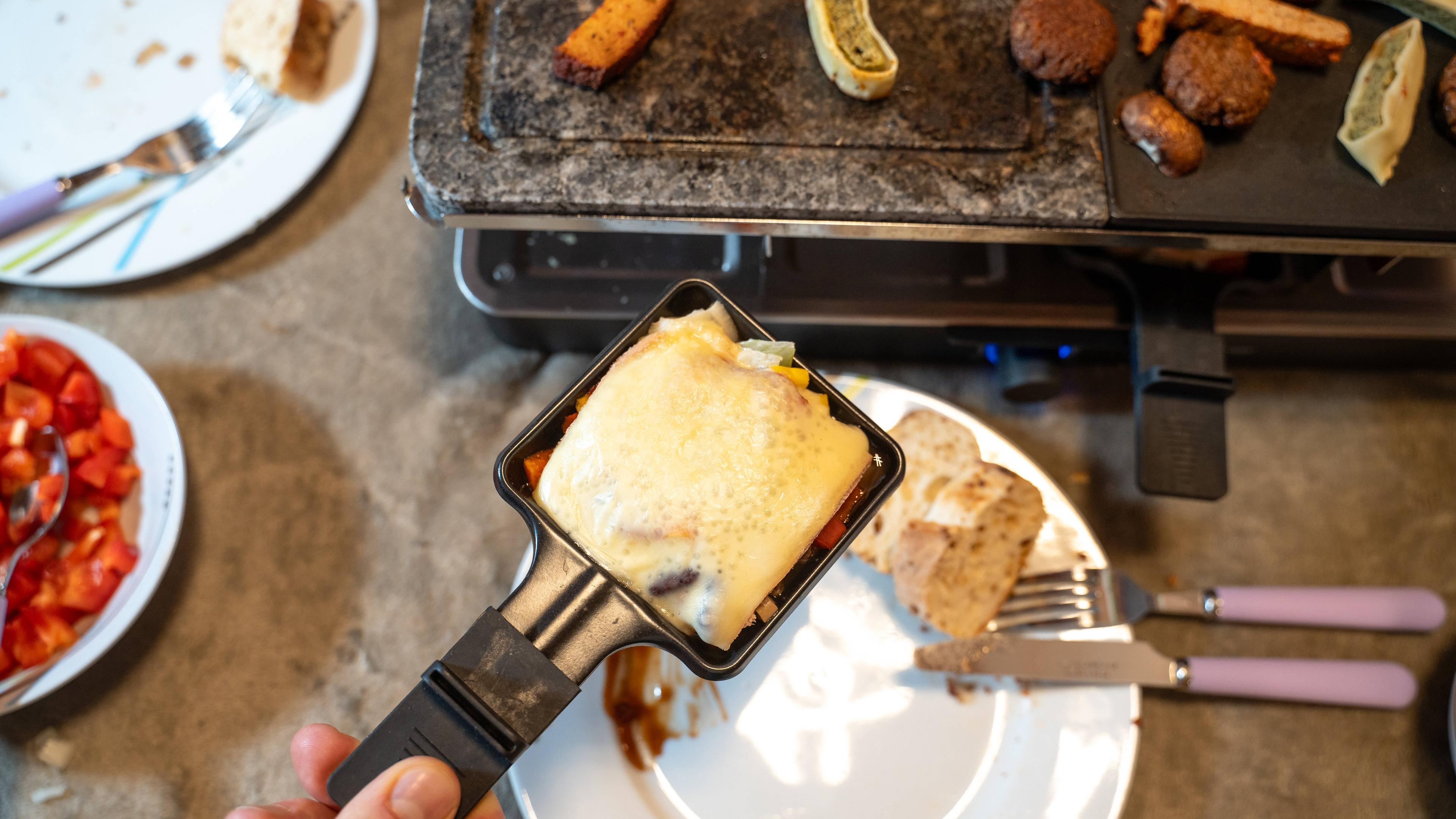 Mann hält Raclette-Pfännchen in der Hand.