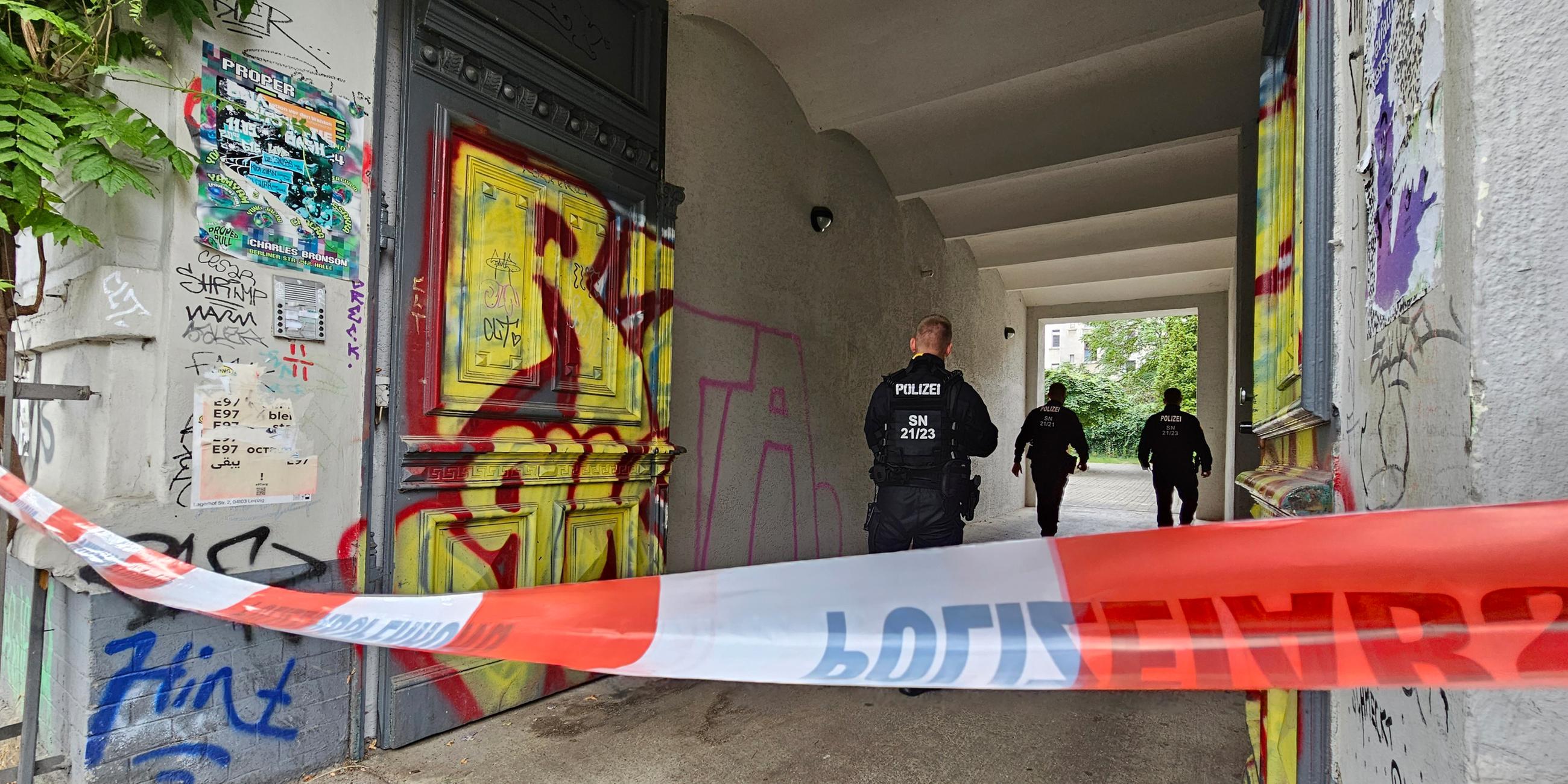 08.08.2024, Sachsen, Leipzig: In einem mit Flatterband abgesperrten Hauseingang gehen drei Polizisten.