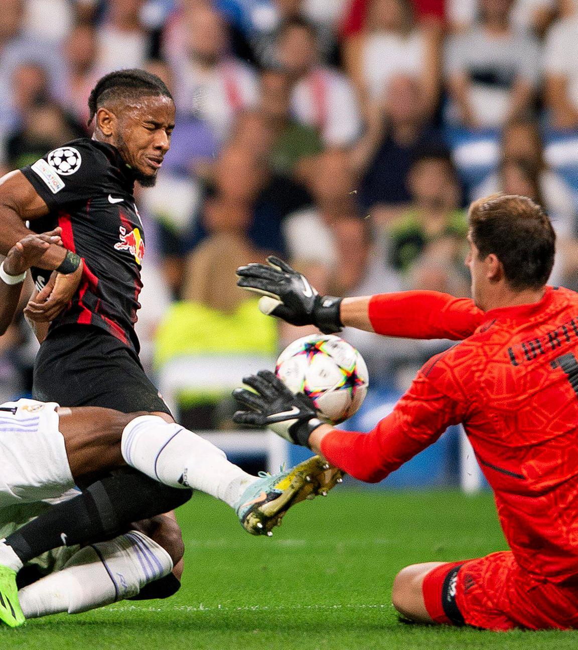 Christopher Nkunku von RB Leipzig und Madrids Torwart Thibaut Courtois und Aurélien Tchouaméni kämpfen um den Ball am 14.09.2022 in Madrid.