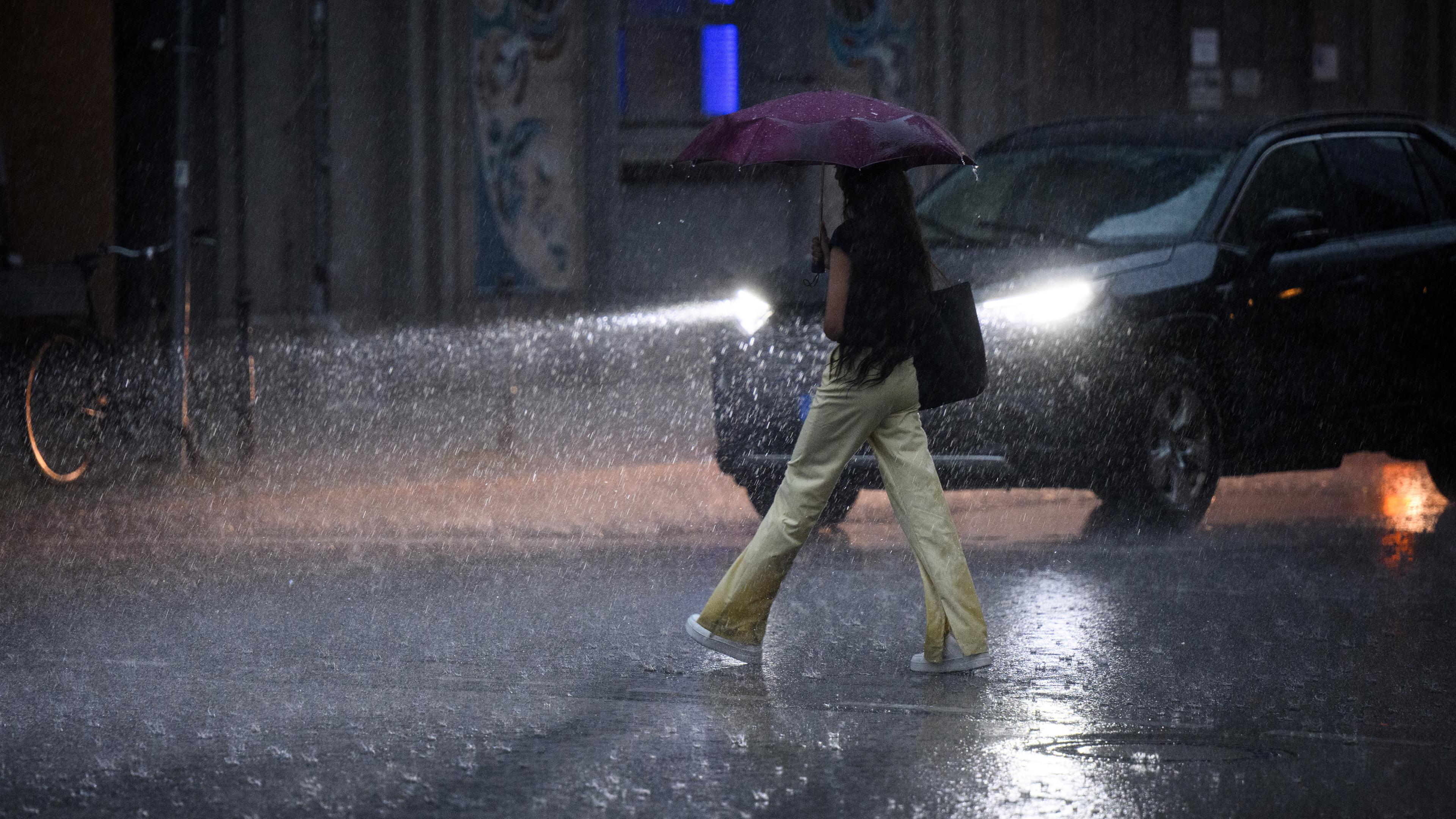 10.07.2024, Berlin: Eine Frau geht am frühen Mittag bei Starkregen über eine Straße in Berlin-Mitte.