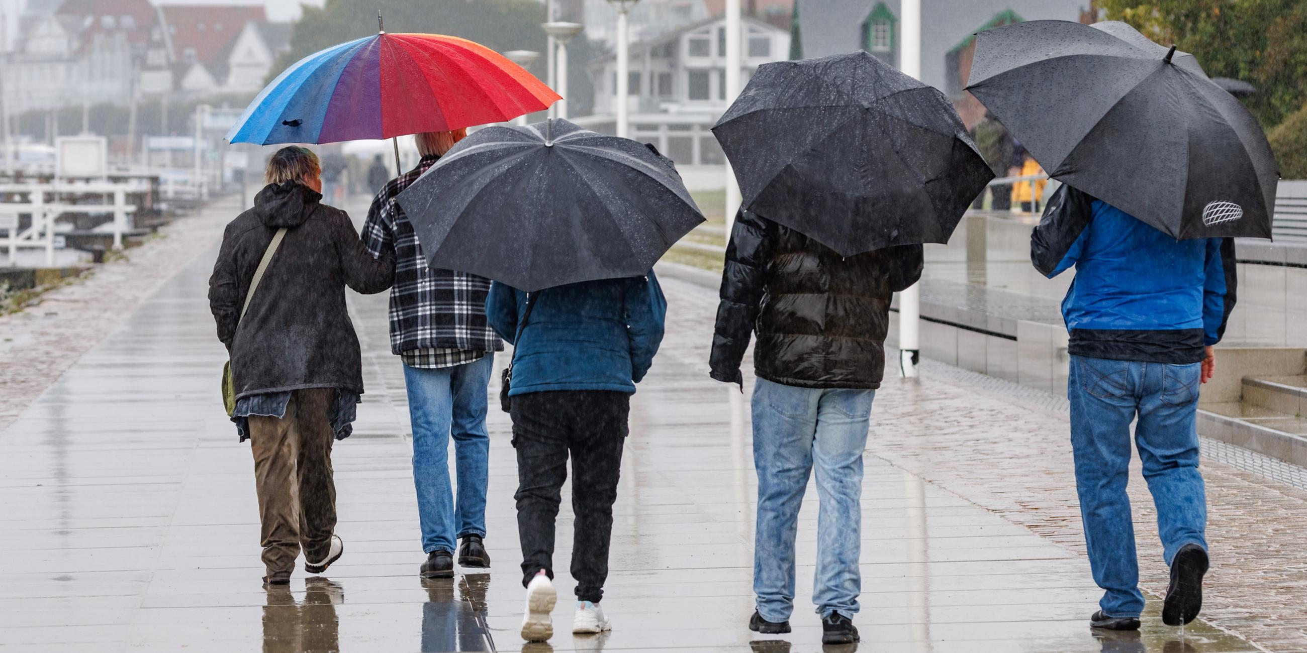 Ausflügler gehen im Regen unter Schirmen auf der Promenade von Travemünde. 