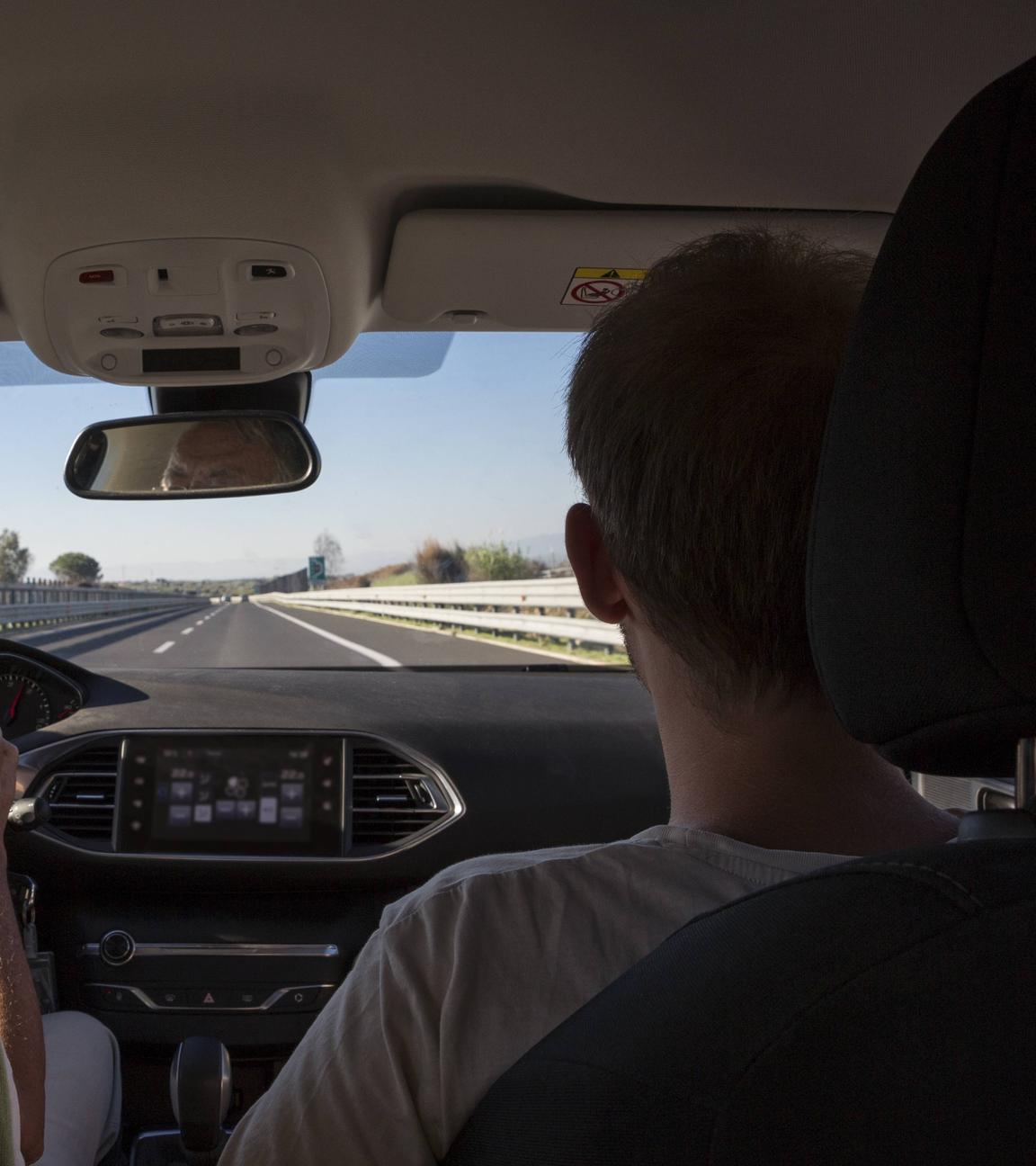 Ein älterer und ein jüngerer Mann sitzen im Auto und fahren auf der Autobahn.