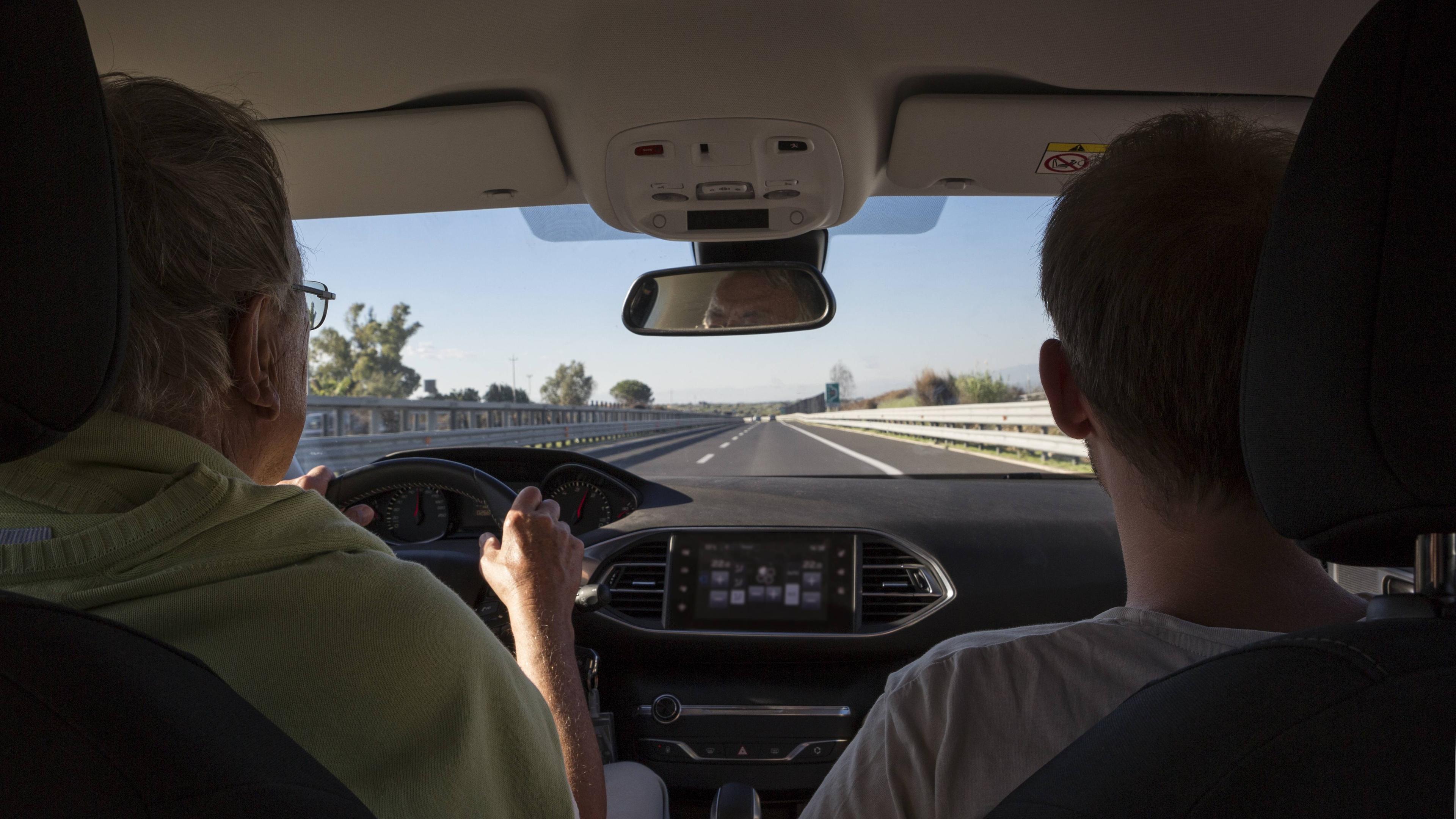 Ein älterer und ein jüngerer Mann sitzen im Auto und fahren auf der Autobahn.
