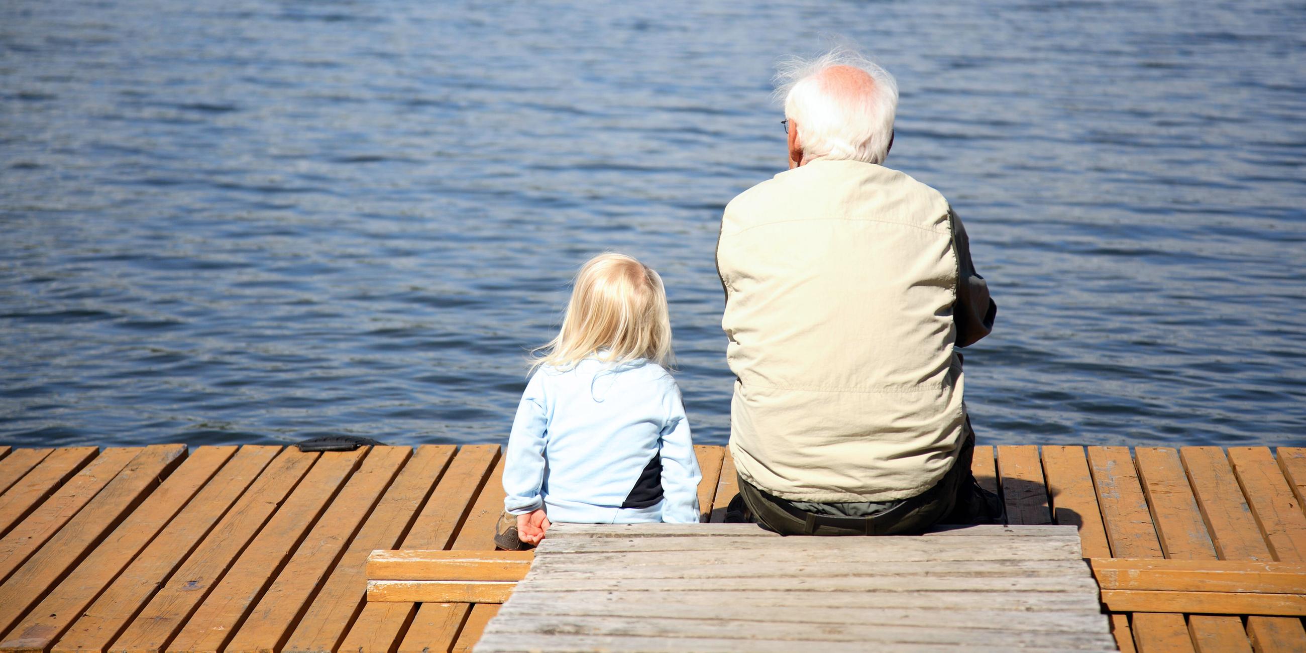 Großvater und Enkelin sitzen am Ufer eines Sees