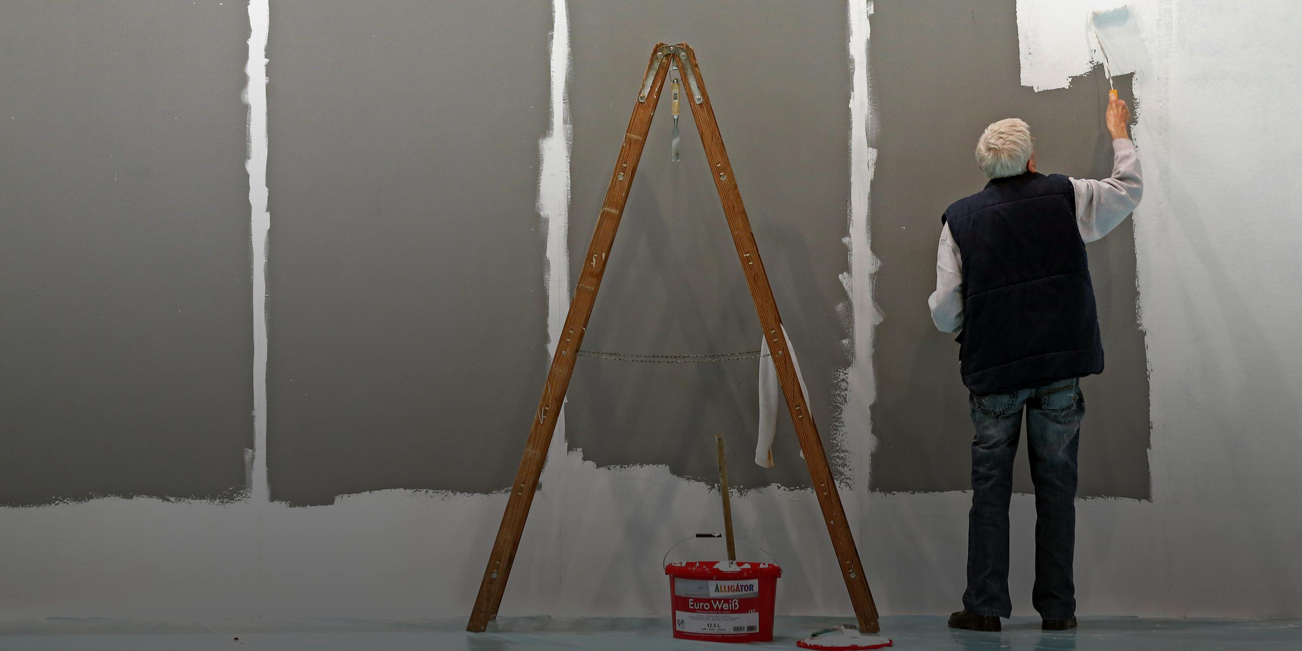 Ein älterer Herr mit grauen Haaren weißt eine Wand