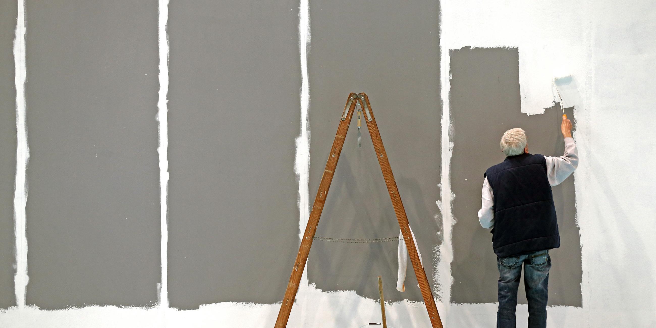 Ein älterer Herr mit grauen Haaren streicht auf der Leipziger Messe eine Wand. Archivbild