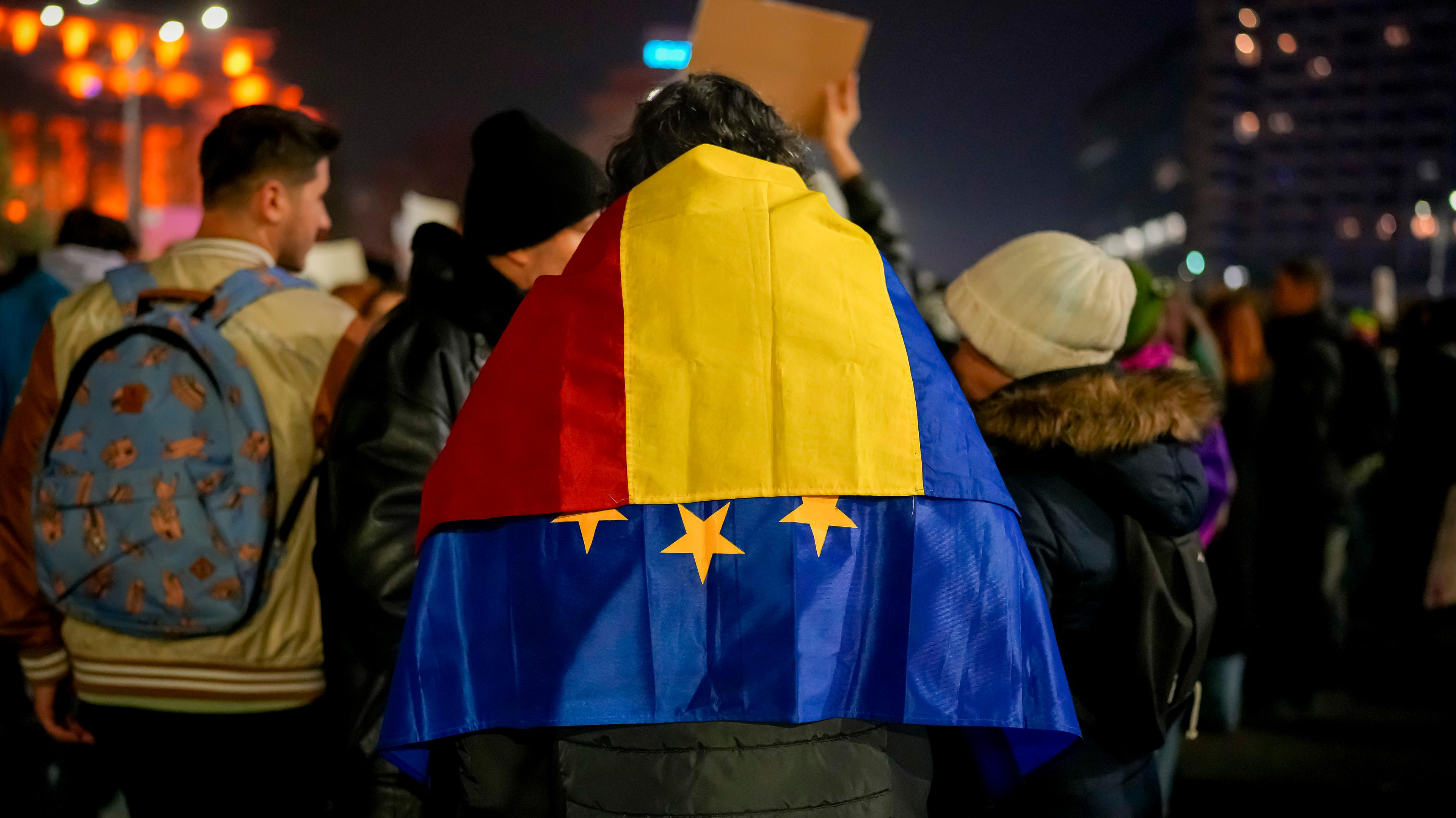 Ein Mann mit der rumänischen und der EU-Fahne über den Schultern nimmt an einem Protest gegen Georgescu, den unabhängigen Kandidaten für das rumänische Präsidentenamt, der die erste Wahlrunde gewonnen hat.