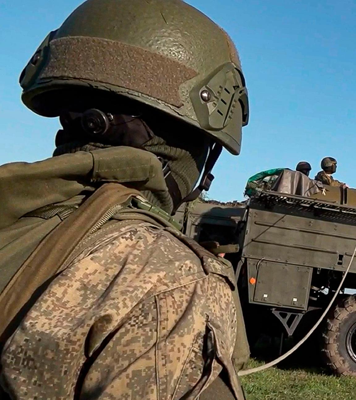 Ein russischer Soldat im Vordergrund bei einer Militärübung, im Hintergrund ein Militärfahrzeug mit Kran.