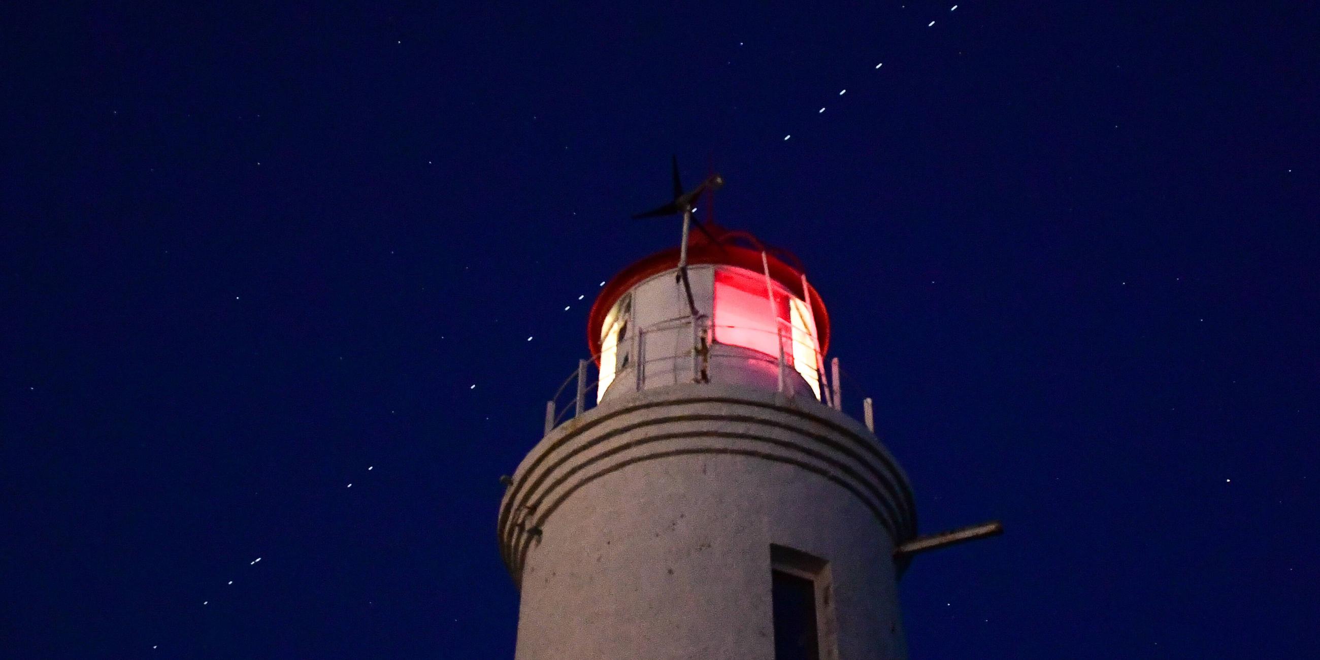 Russland, Wladiwostock: EIne Kette von Starlink Satelliten ist über einem Leuchtturm zu sehen