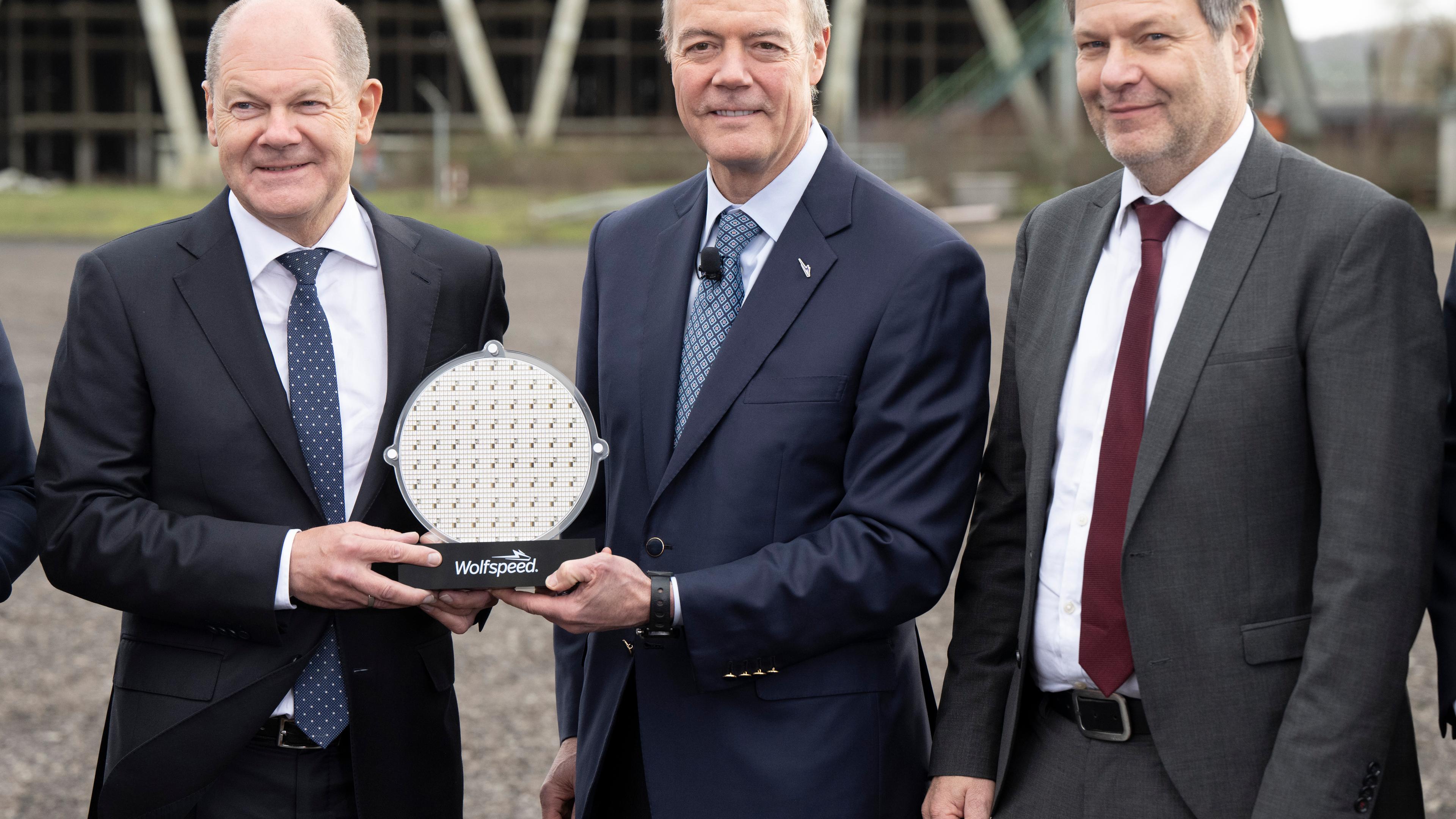 Saarland, Ensdorf: Bundeskanzler Olaf Scholz (l-r, SPD) und Gregg Lowe, CEO von Wolfspeed, und Robert Habeck (Bündnis 90/Die Grünen), Bundesminister für Wirtschaft und Klimaschutz, halten auf einer Veranstaltung am künftigen Standort der Wolfspeed-Chipfabrik in Ensdorf im Saarland einen Wafer.