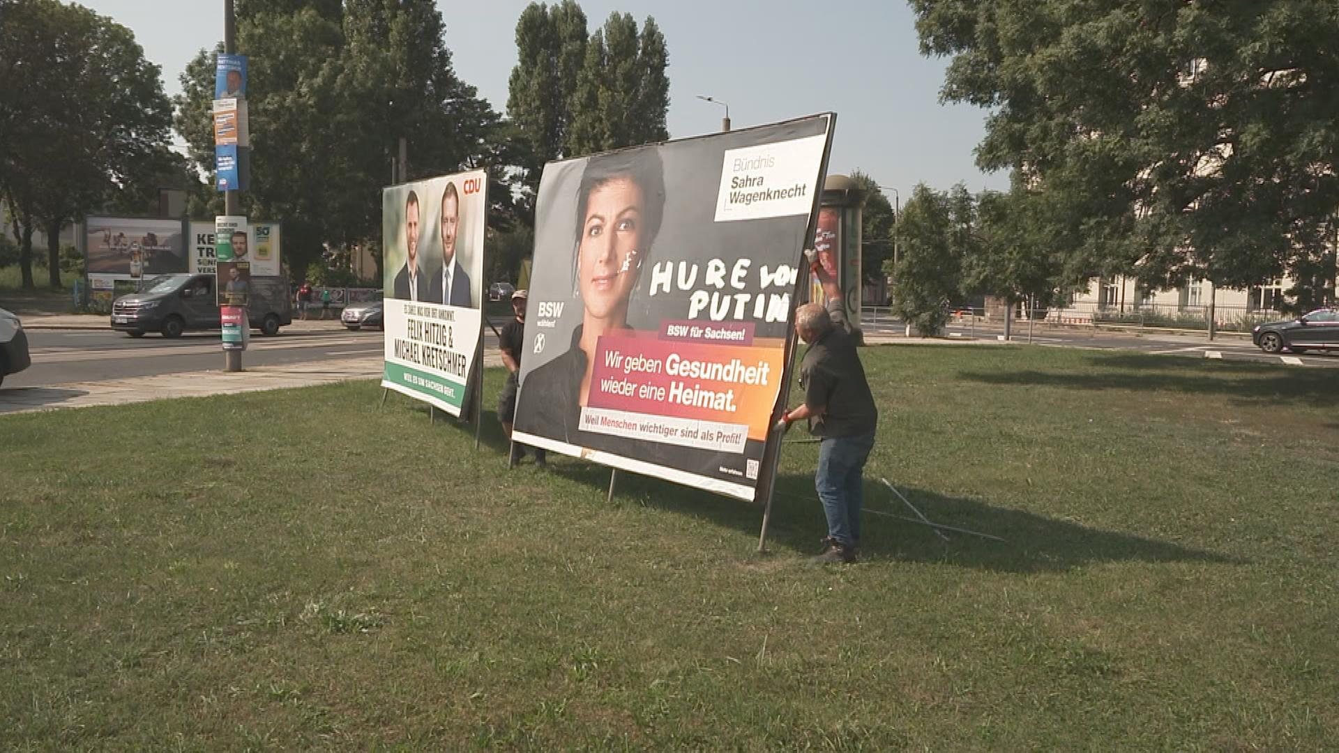 Zwei Männer bauen in Dresden ein Wahlplakat vom BSW ab