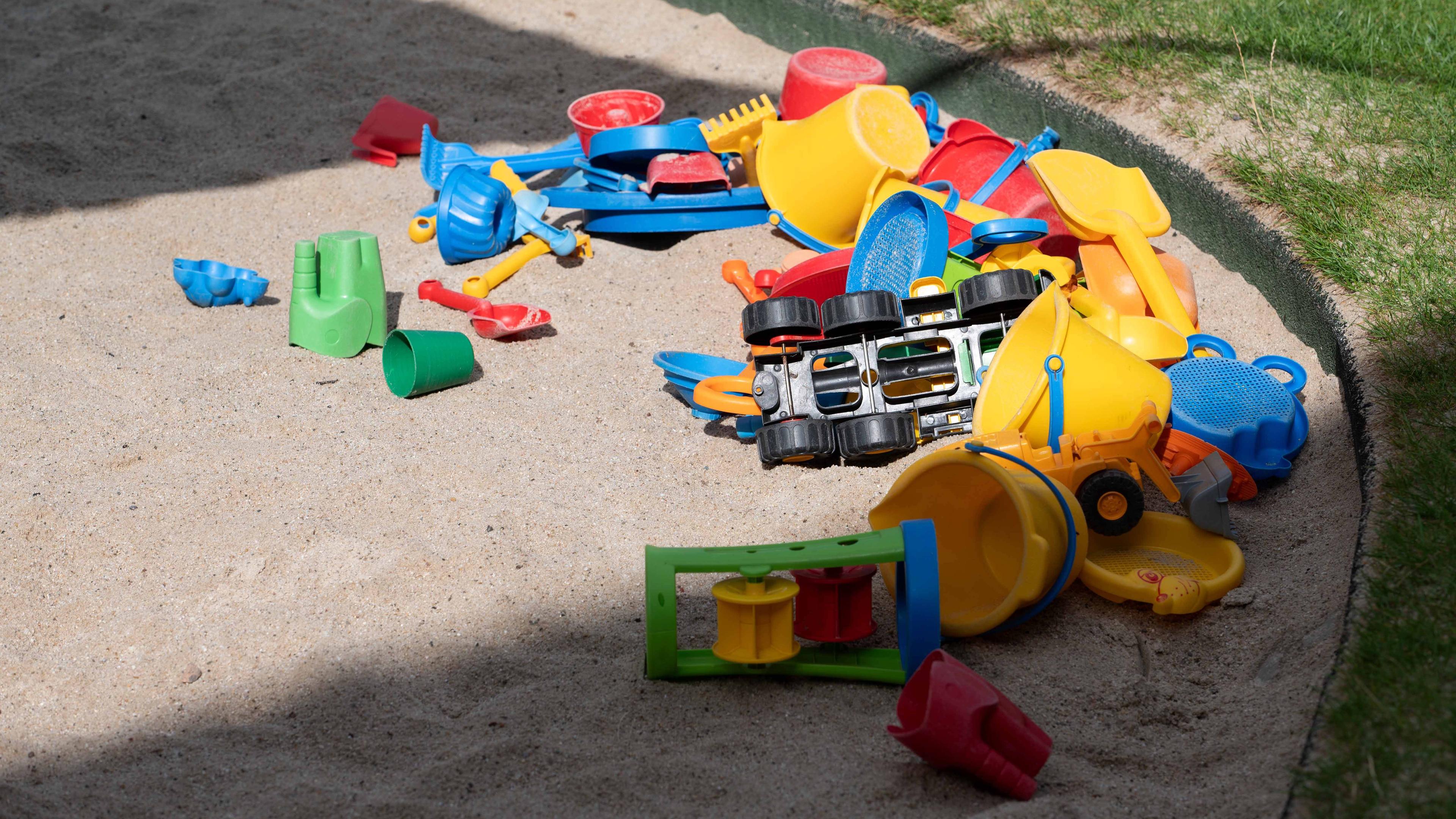 Viele Sandspielsachen, Förmchen und Schaufel liegen in einem Sandkasten.