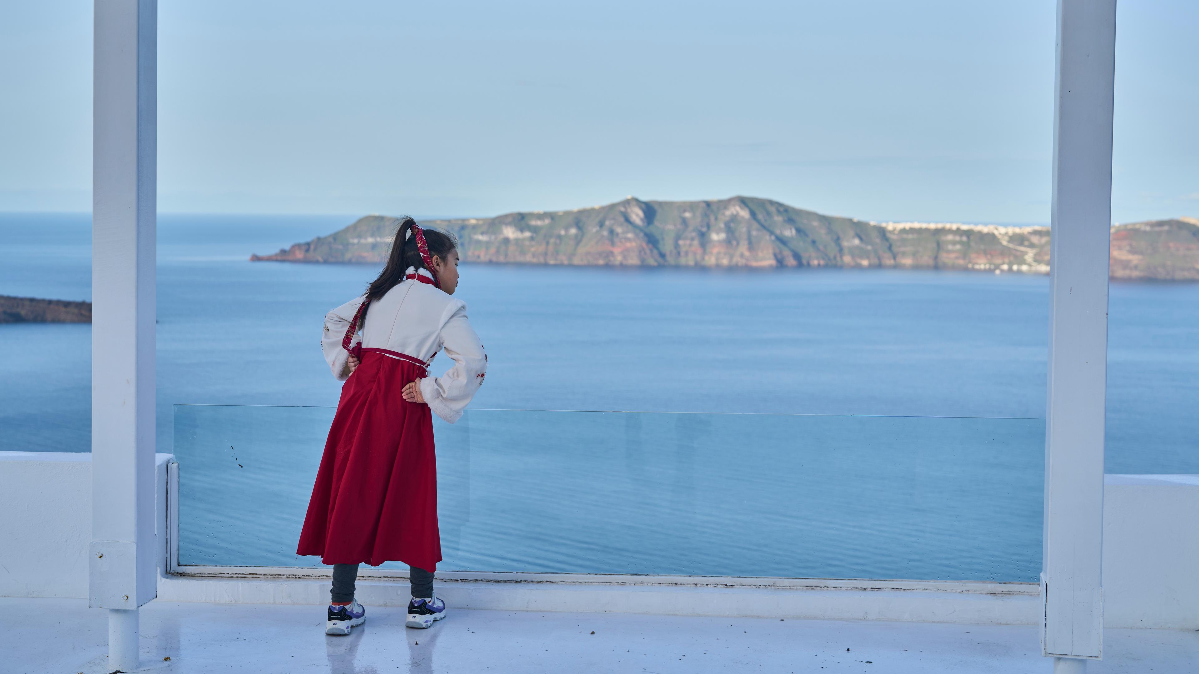 dpatopbilder - 04.02.2025, Griechenland, Santorin: Eine Frau aus China blickt von einer Caldera bei Firostefani auf die Insel Therasia, während die Behörden Notfallmaßnahmen als Reaktion auf intensive seismische Aktivitäten auf der beliebten Ägäis-Ferieninsel Santorini ergreifen. Foto: Petros Giannakouris/AP/dpa +++ dpa-Bildfunk +++