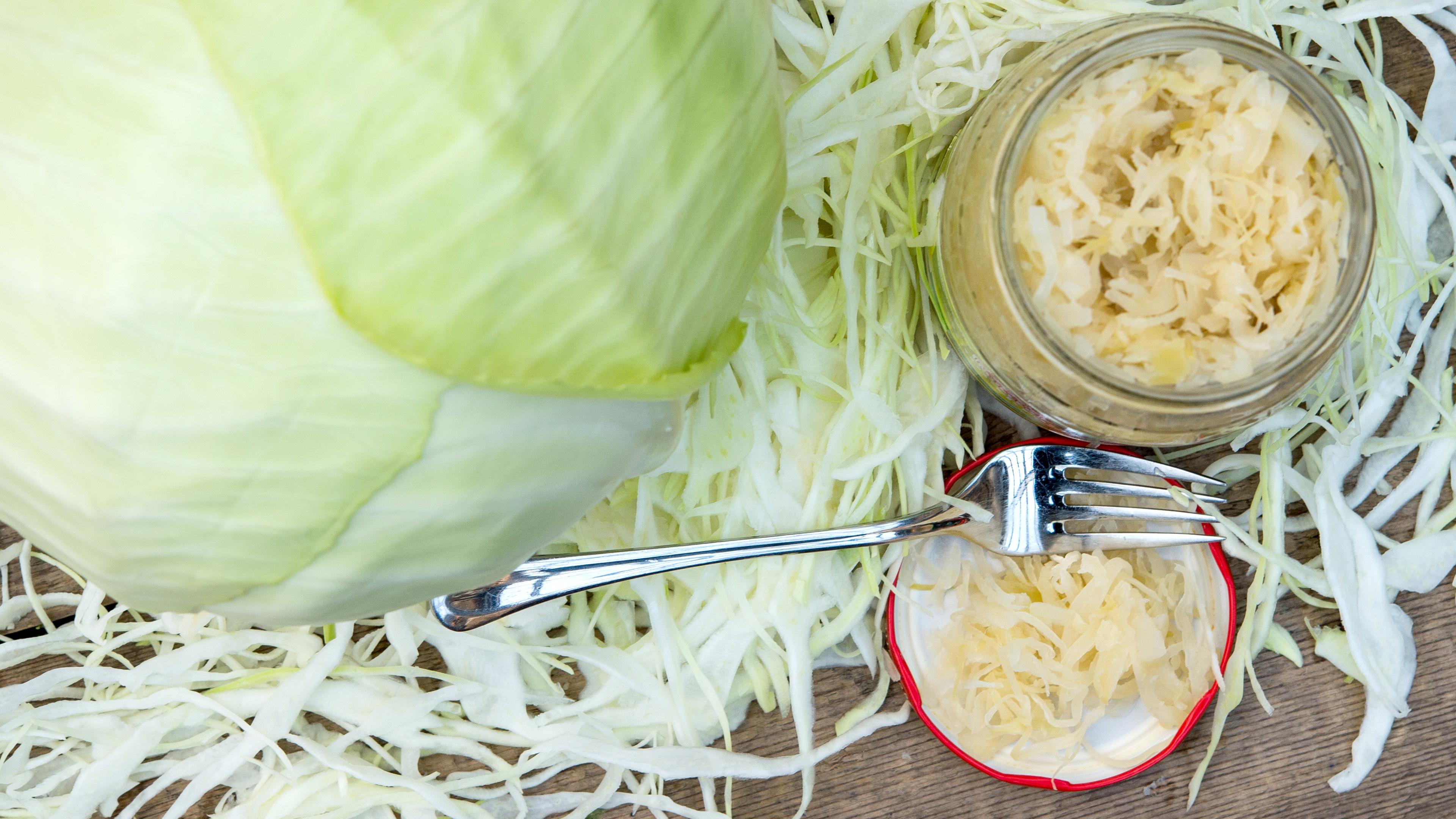 Ein Weißkohl-Kopf wird zusammen mit Sauerkraut im Einweckglas präsentiert.