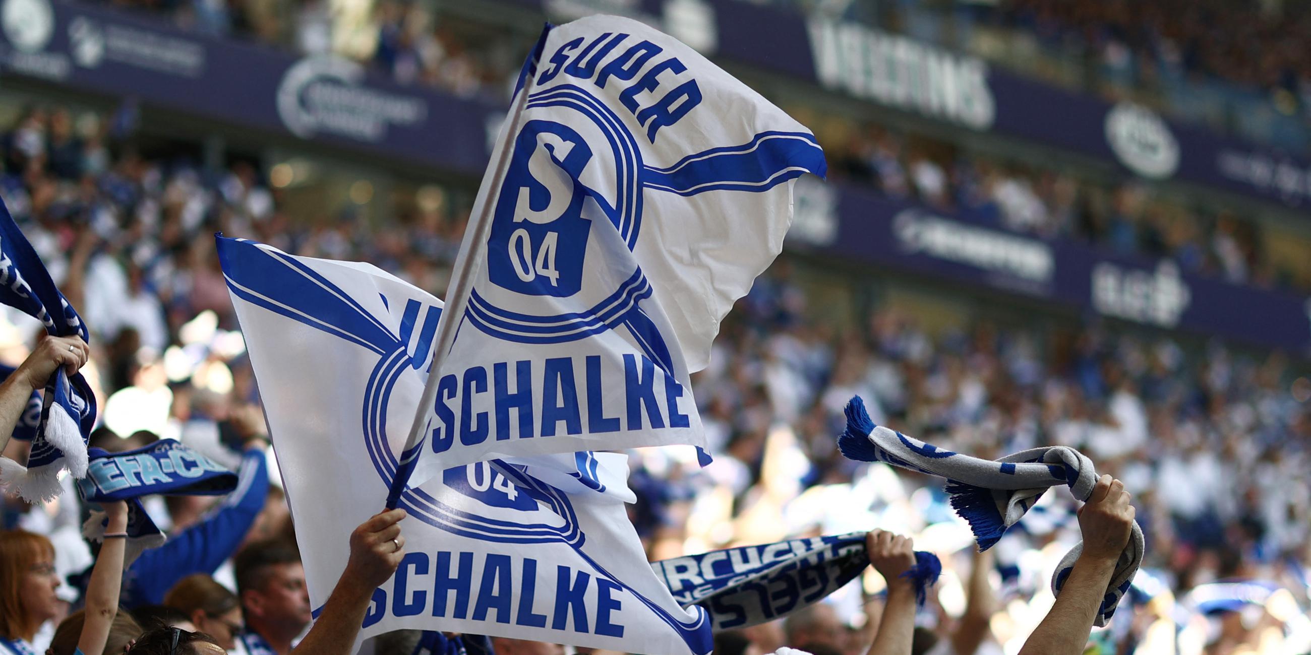 In einem Stadion steht eine Menschenmenge und hält blau-weiße Schalke Fahnen und Schals.