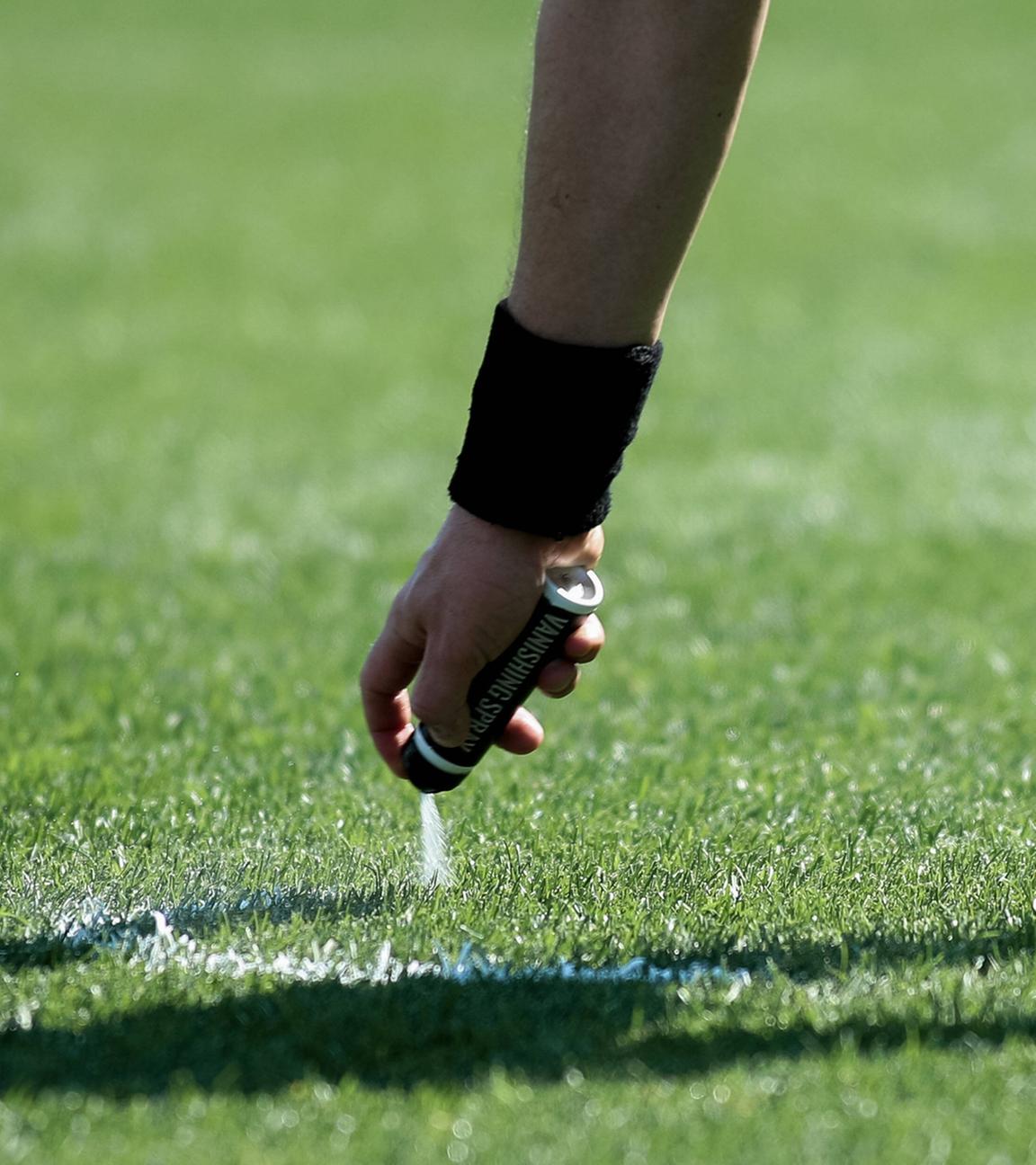 Ein Schiedsrichter sprüht die Freistoßlinie mit Sprühschaum auf den Rasen
