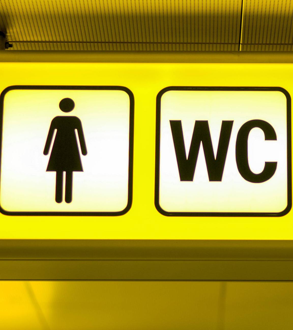Großaufnahme eines gelben Hinweis-Schildes WC mit Pfeil in Richtung der Damentoilette.