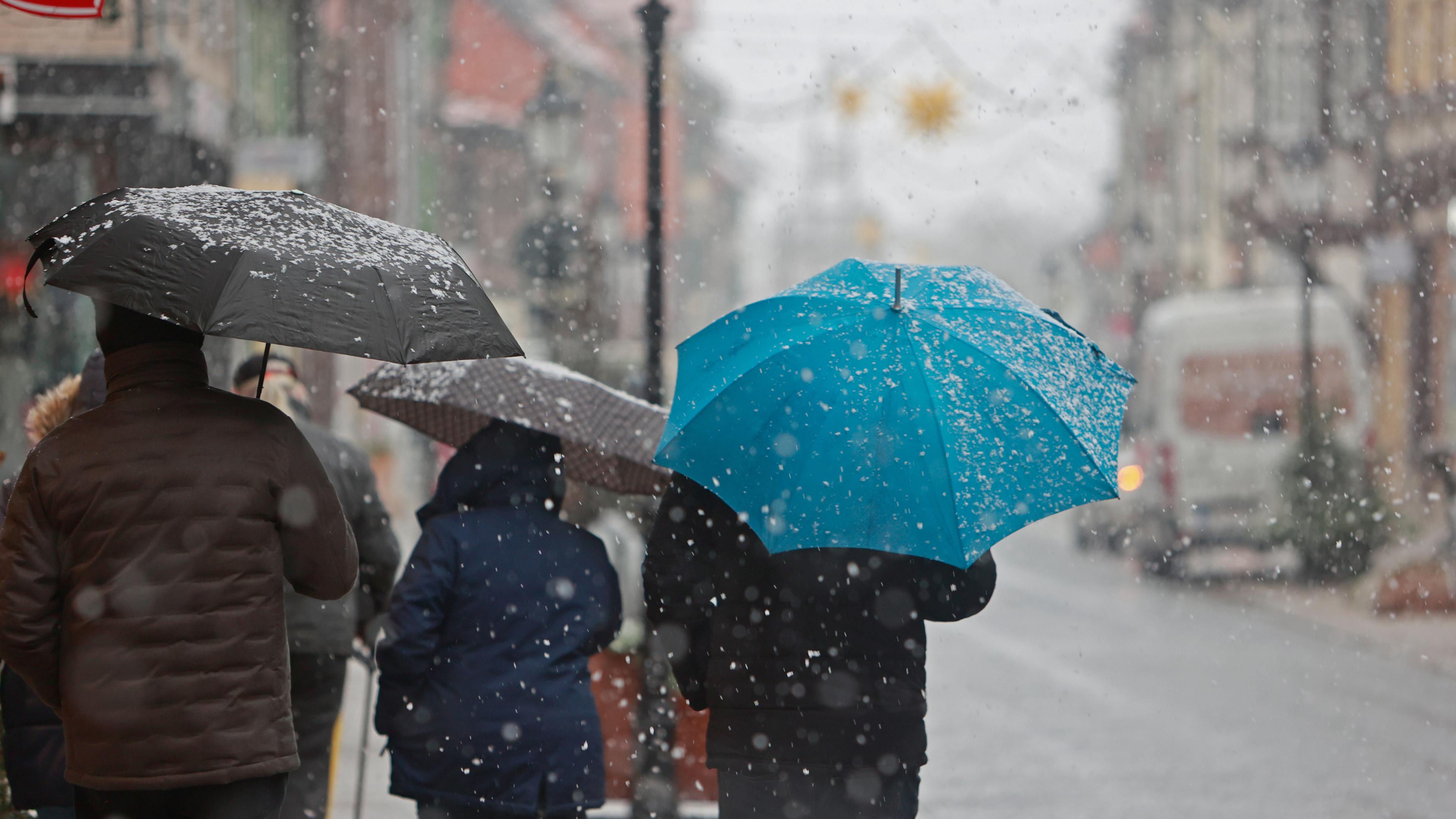 Sachsen-Anhalt, Wernigerode: Menschen gehen mit Regenschirm bei Schneeregen am Montagvormittag durch die Innenstadt von Wernigerode.