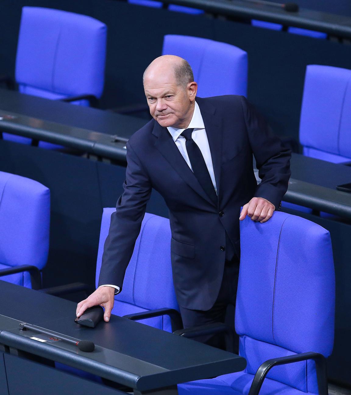 Bundeskanzler Olaf Scholz (SPD) hält sich an einem Stuhl auf der Regierungsbank fest.