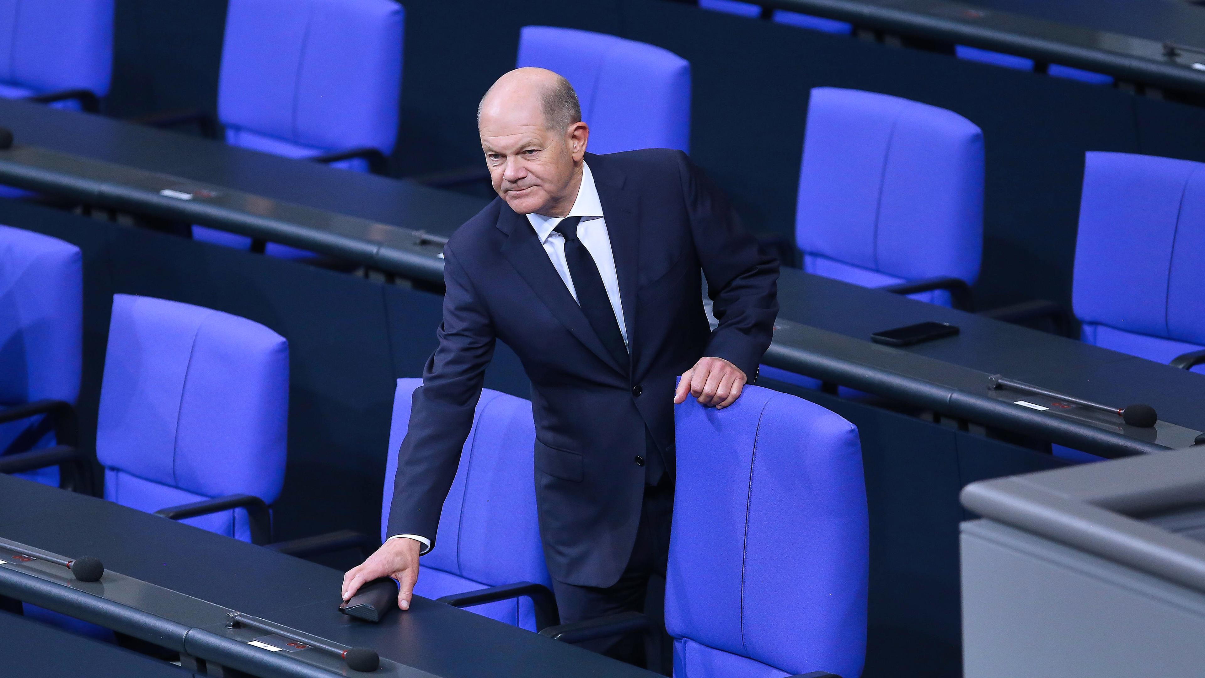 Bundeskanzler Olaf Scholz (SPD) hält sich an einem Stuhl auf der Regierungsbank fest.