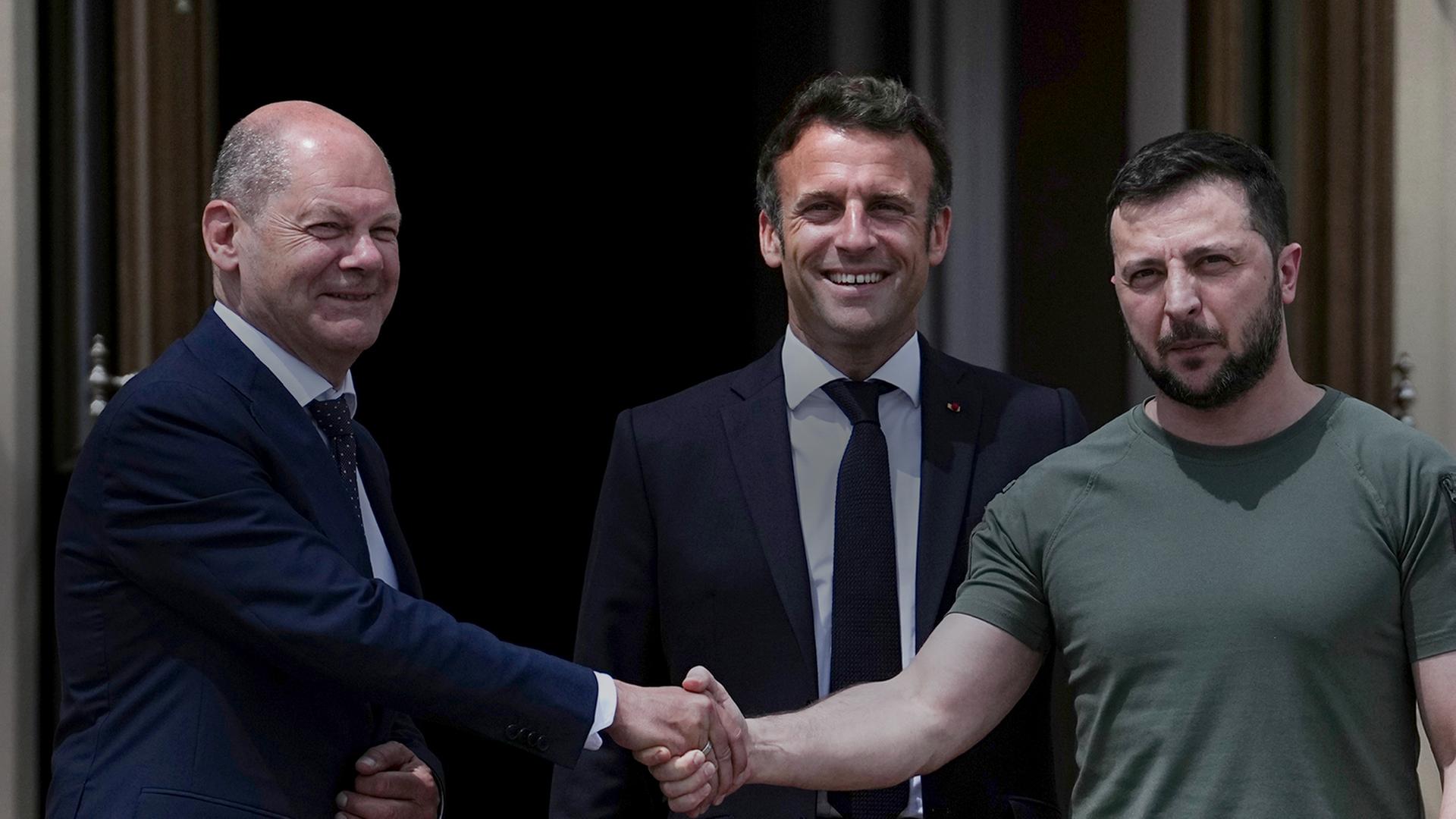 Zu sehen sind von links nach rechts, Bundeskanzler Scholz, Frankreichs Präsident Macron und der Präsidenten Selenskyj in Kiew. Scholz und Selenskyj reichen sich die Hand, Macron steht in der mitte hinter den Beiden.