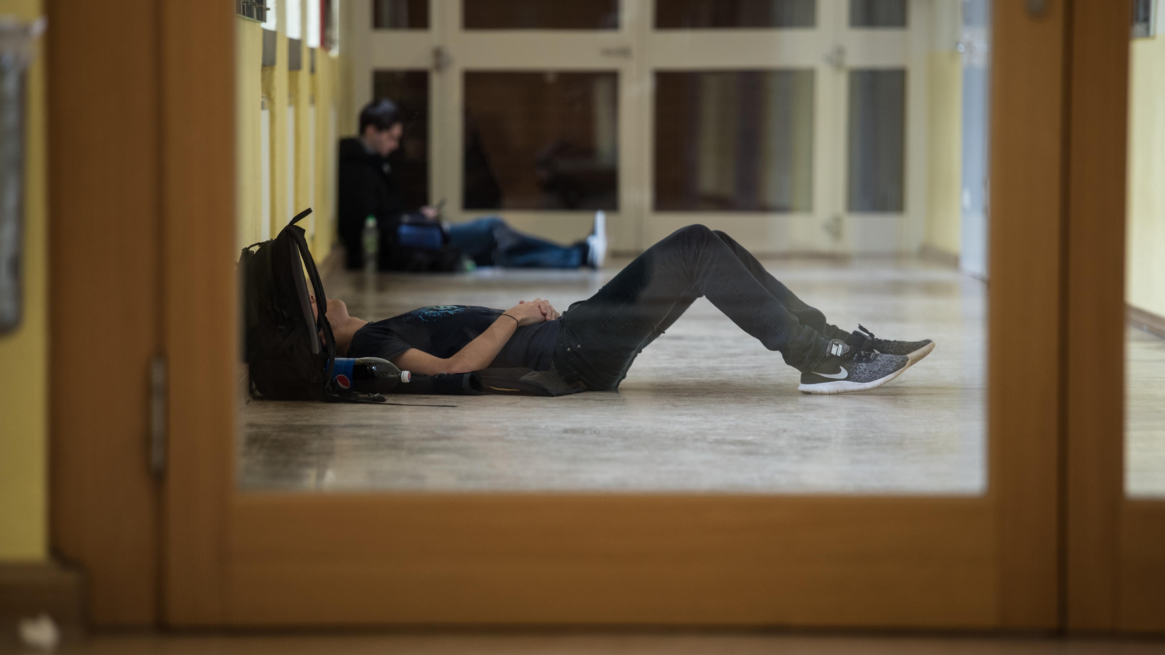 Schüler liegt schlafend im Gang einer Schule