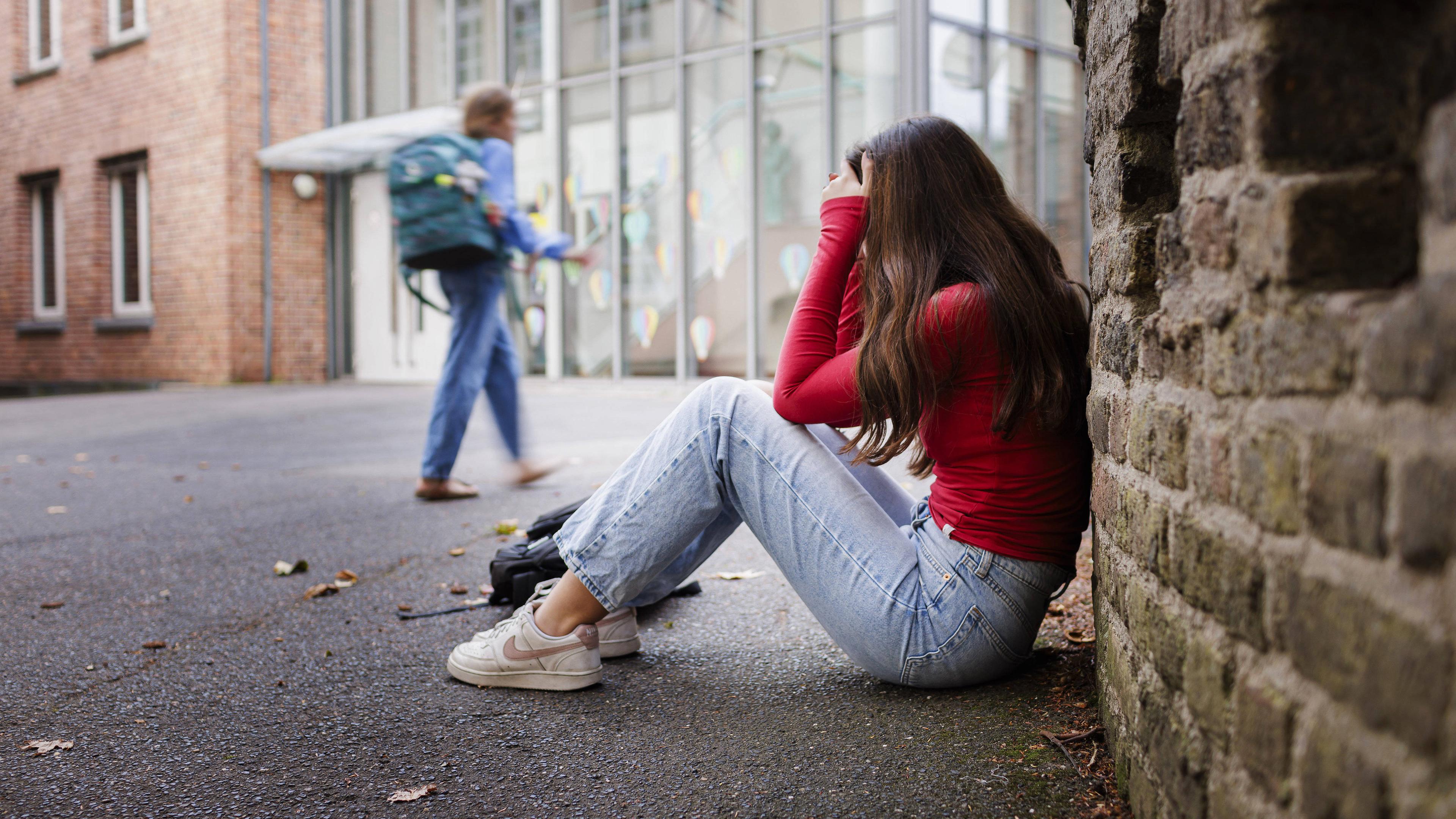 Illustration: Eine Schülerin sitzt frustriert auf dem Boden des Schulhofes in Bonn