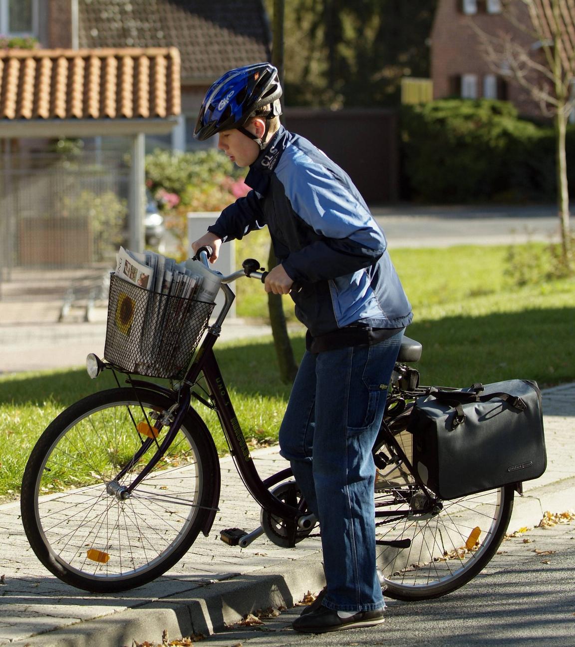 Ein Schüler liefert mit einem Fahrrad Zeitungen aus.