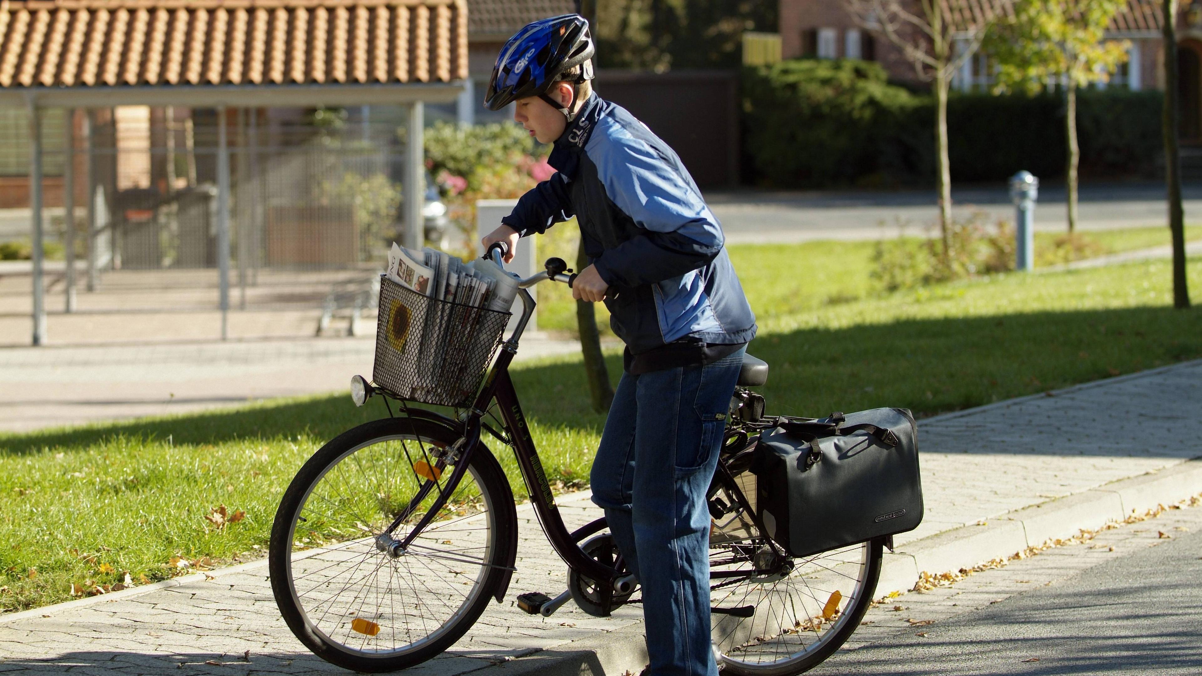 Ein Schüler liefert mit einem Fahrrad Zeitungen aus.