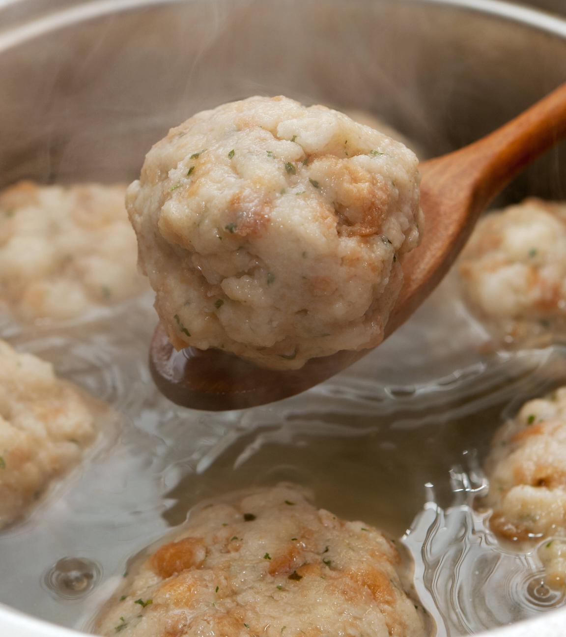 Ein Semmeknödel wird mit einem Kochlöffel aus einem Kochtopf gehoben.