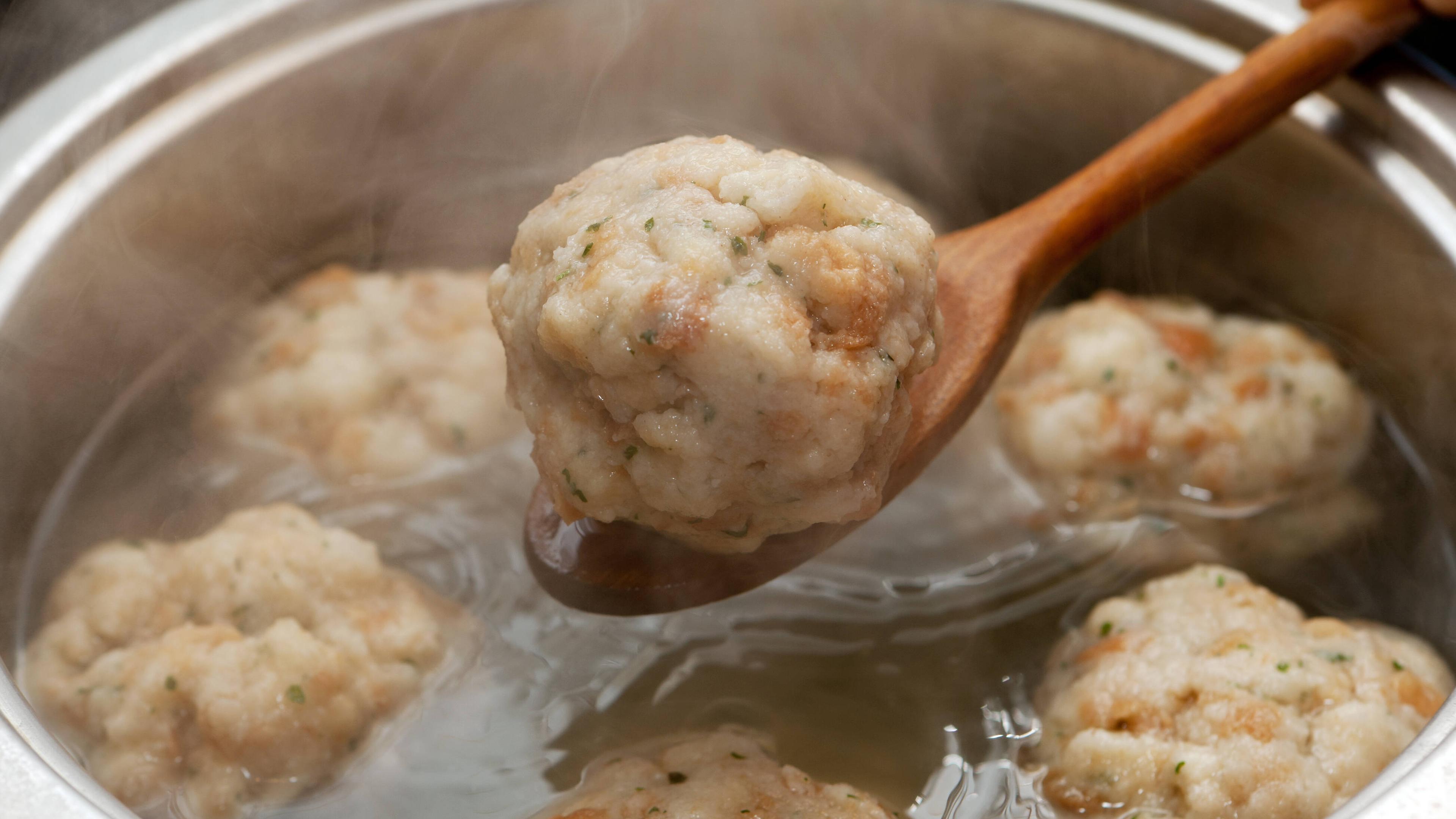 Ein Semmeknödel wird mit einem Kochlöffel aus einem Kochtopf gehoben.