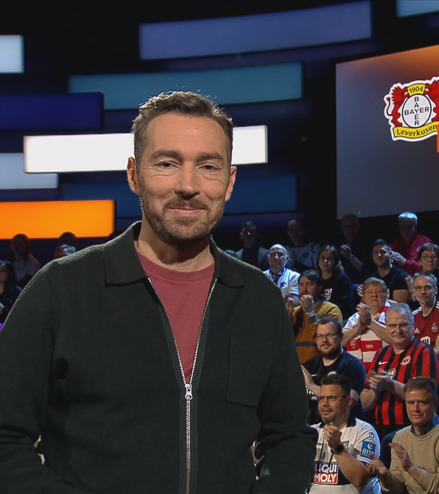 Der Moderator Sven Voss steht im aktuellen Sportstudio. Im Hintergrund wird das Topspiel des Tages angezeigt.