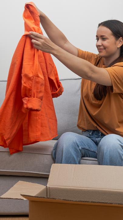 Eine Frau sitzt auf dem Sofa und packt eine Jacke aus einem Paket aus.