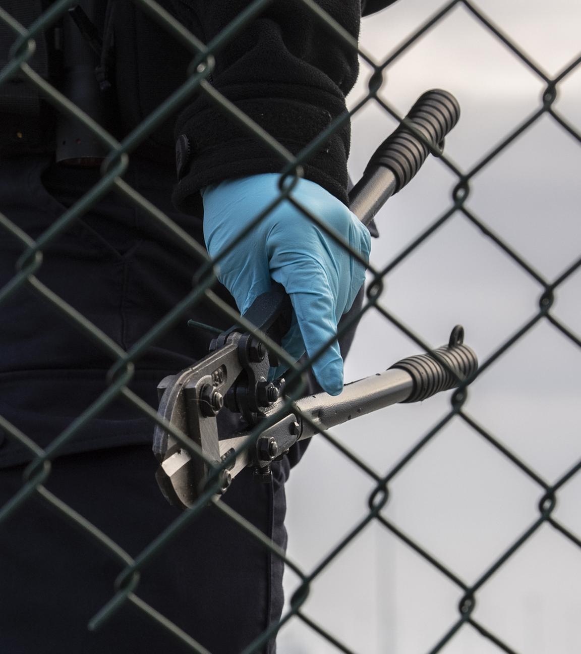 Eine Beamtin der Bundespolizei steht mit einem sichergestellten Bolzenschneider an einem Zaun am BER-Flughafen.