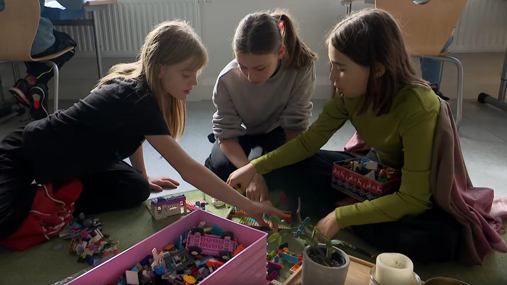 Kinder sitzen zusammen an einem Tisch, sie schreiben und sind am Laptop