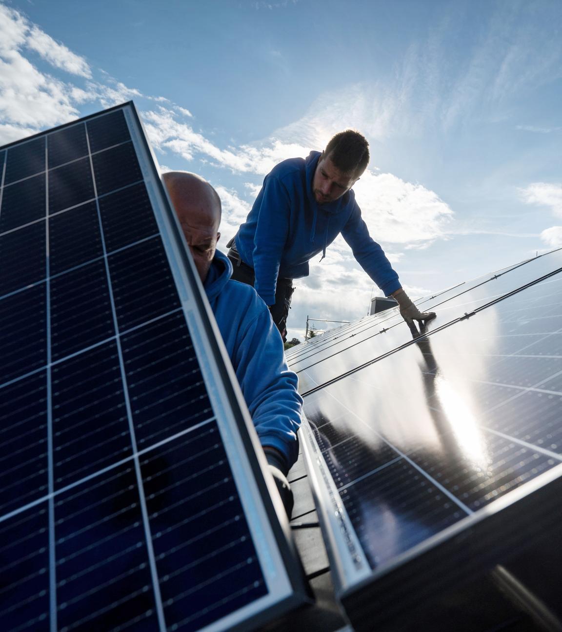 Mitarbeiter einer Firma montieren Photovoltaikmodule auf dem Dach eines Wohnhauses.