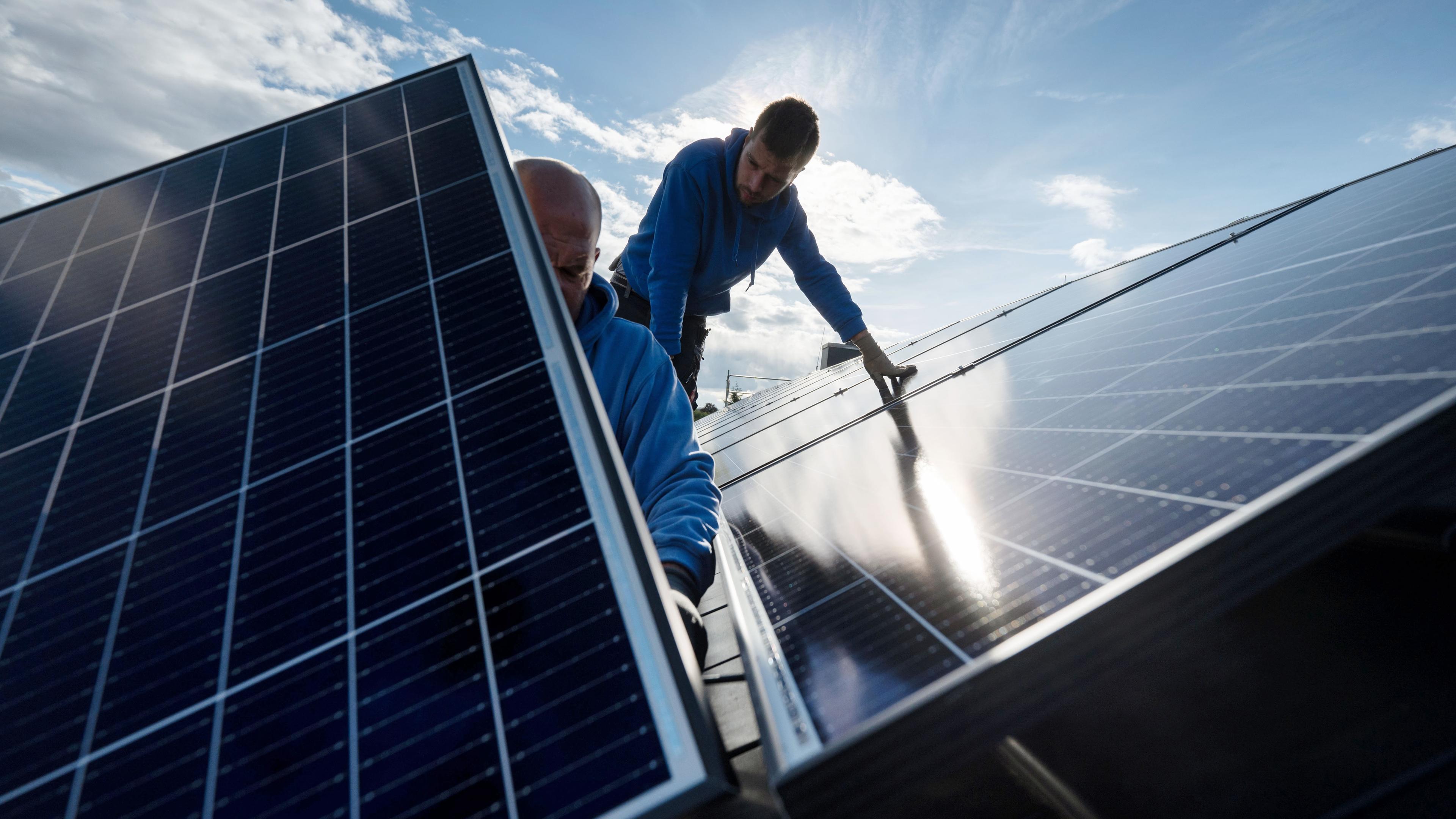 Mitarbeiter einer Firma montieren Photovoltaikmodule auf dem Dach eines Wohnhauses.