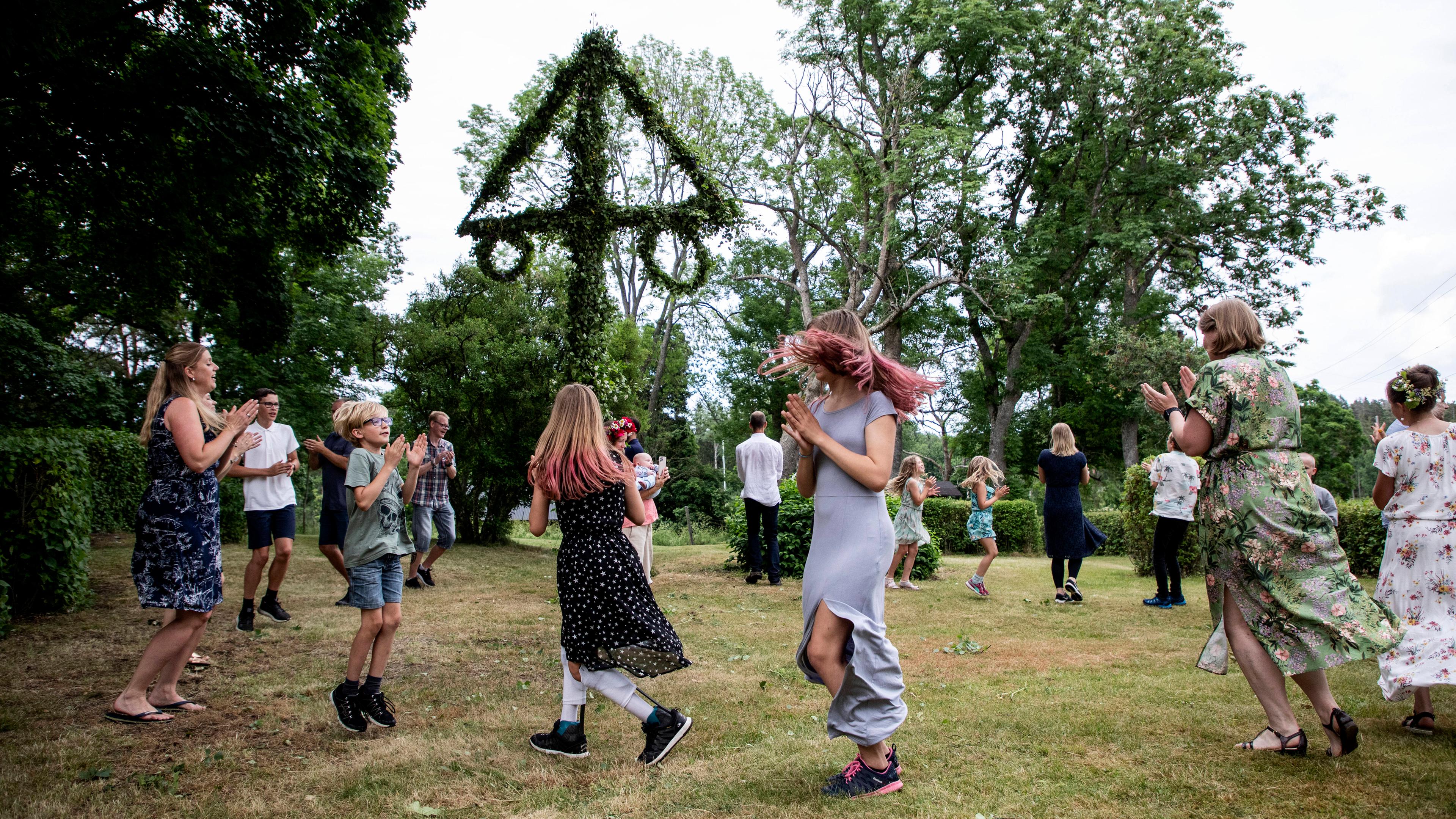 Feiernde tanzen um Mittsommerbaum in Schweden