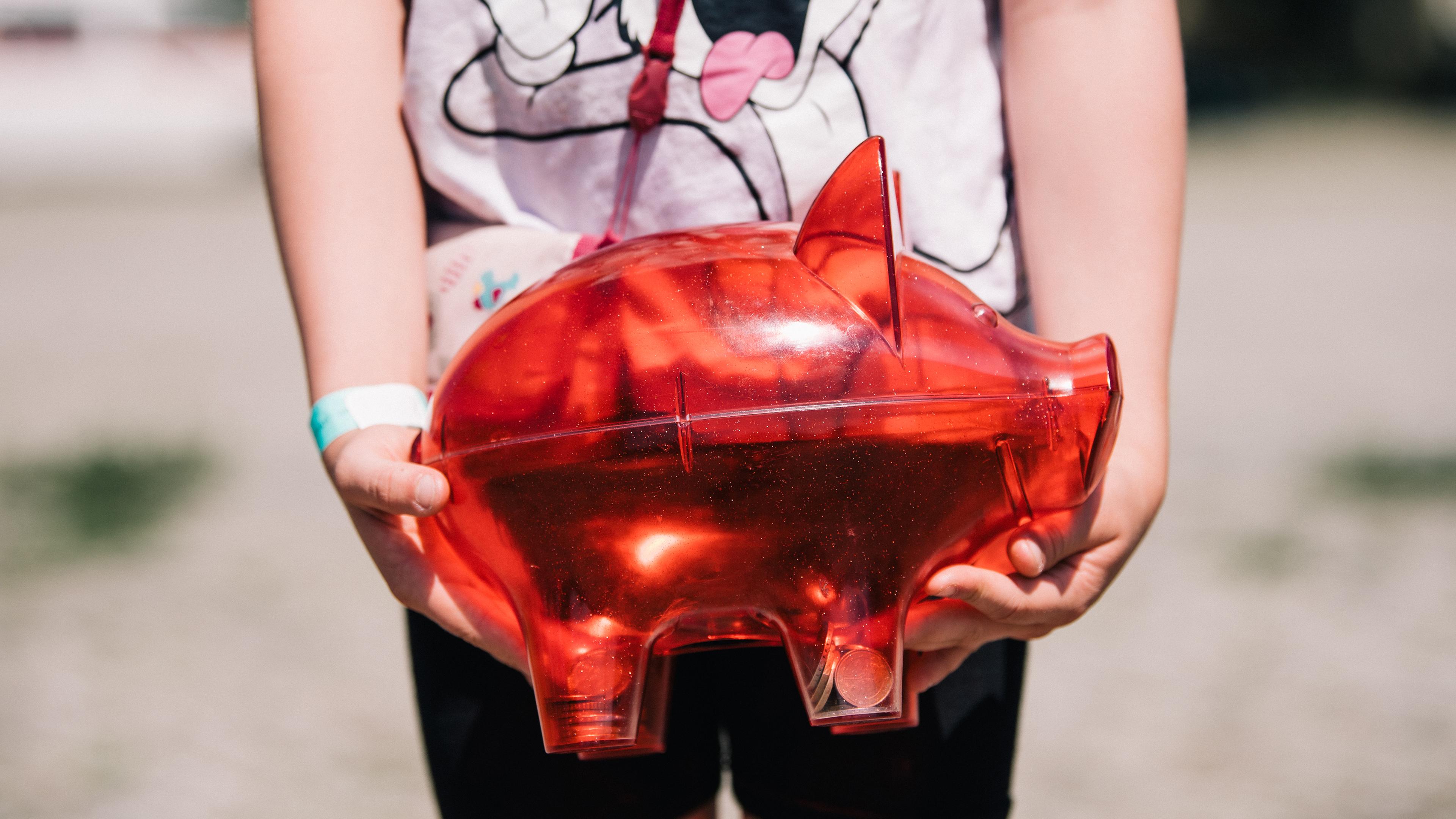Ein Kind hält ein rotes Sparschwein in den Händen.
