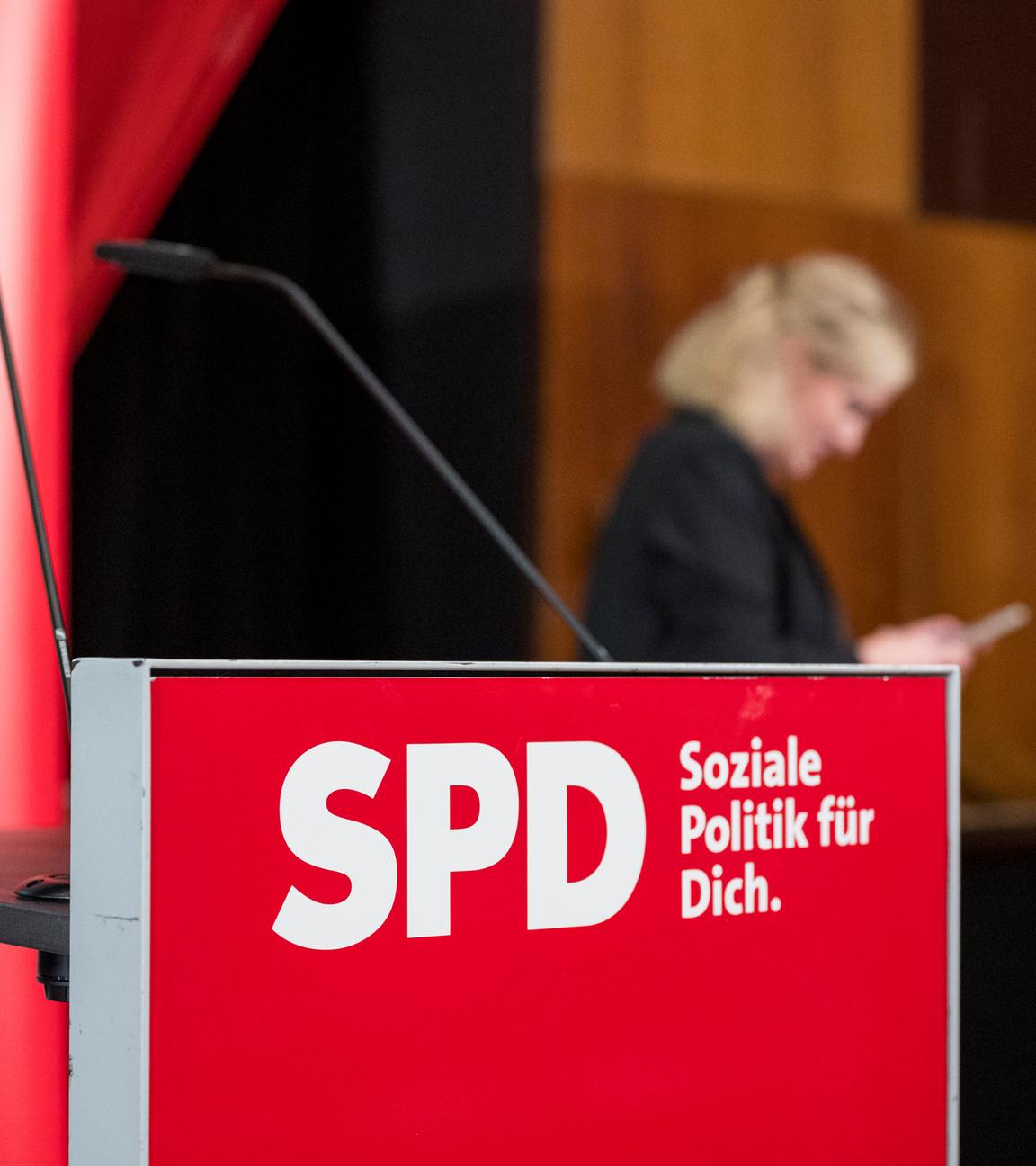 SPD-Rednerpult mit verschwommener Frau und SPD-Plakat im Hintergrund