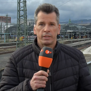 ZDF-Korrespondent Stefan Schlösser. Im Hintergrund ist ein Bahnhof zu sehen.